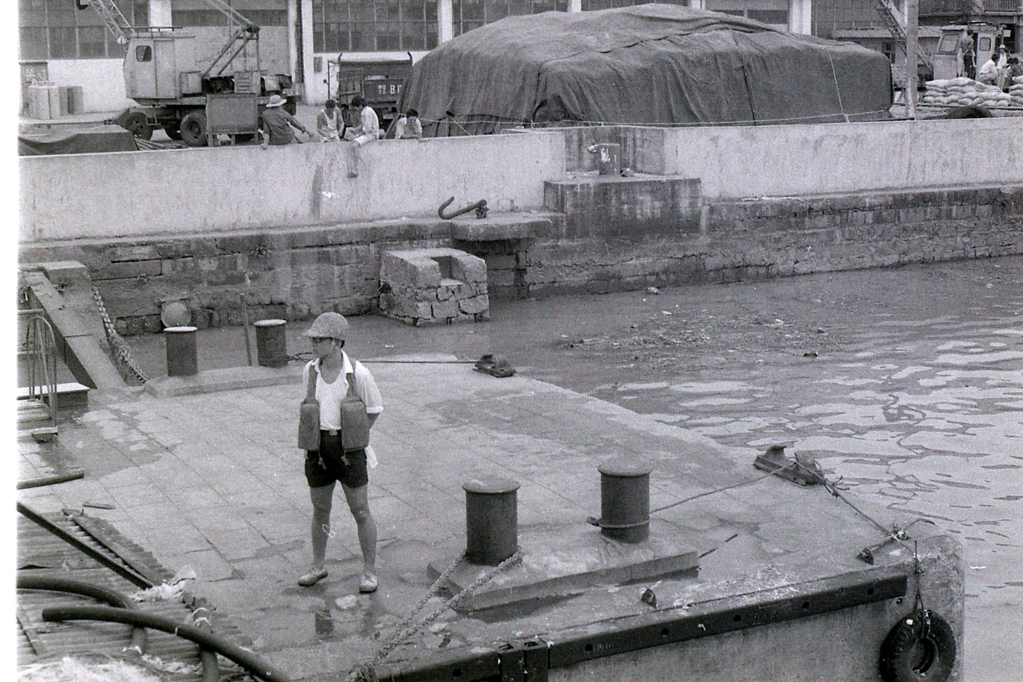 23/7/1989: 26: man untying our ship at Ningbo with bamboo helmet