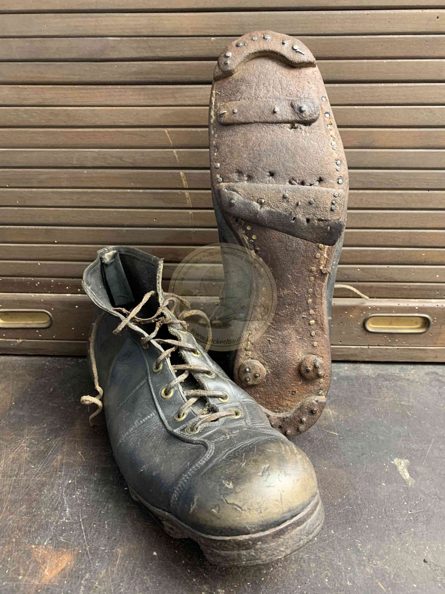 Alte hohe Fußballschuhe mit Rundstollen, Stoppern vorne und hinten und Stegen in schwarzem Leder