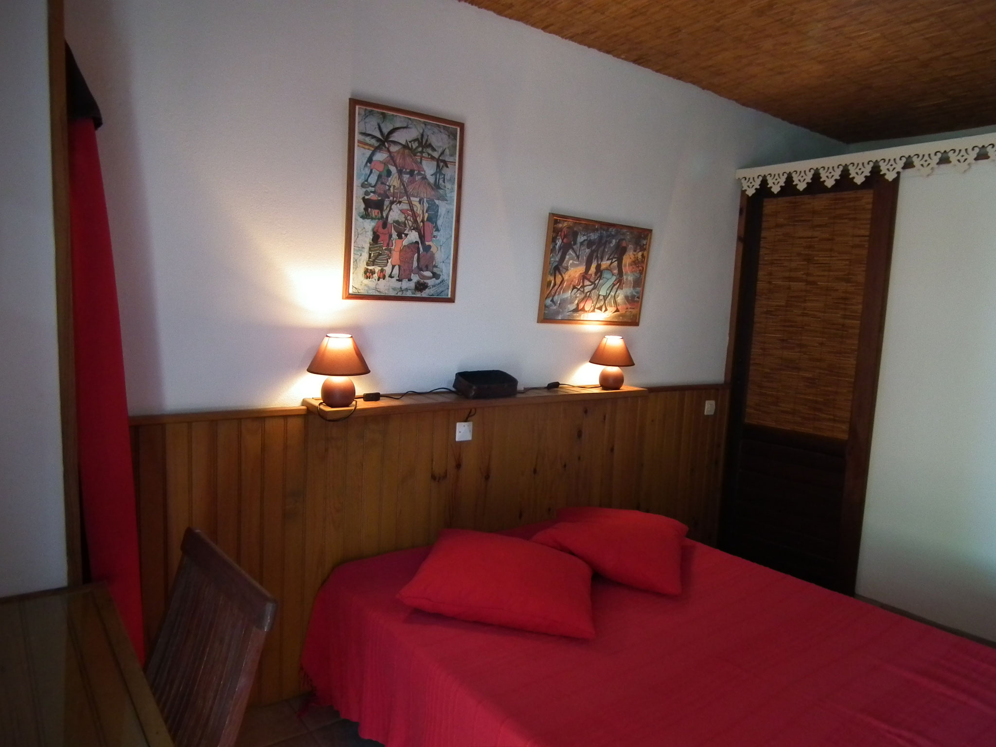 Chambre n°5 – lit rouge, détail décoration artistique, chevet et lampe