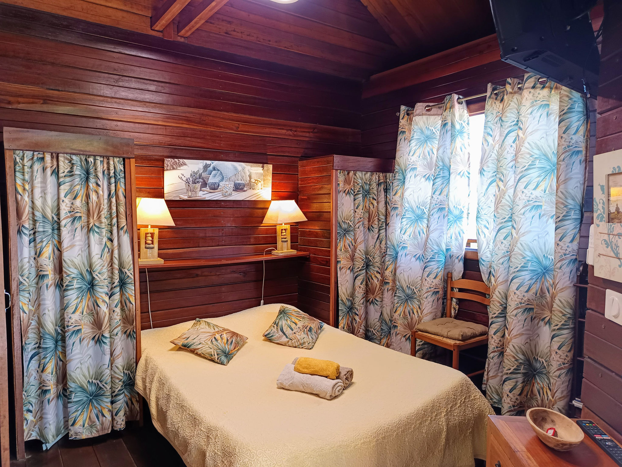Chambre bungalow n°3 – lit double, couvre-lit fleuri, boiserie chaleureuse