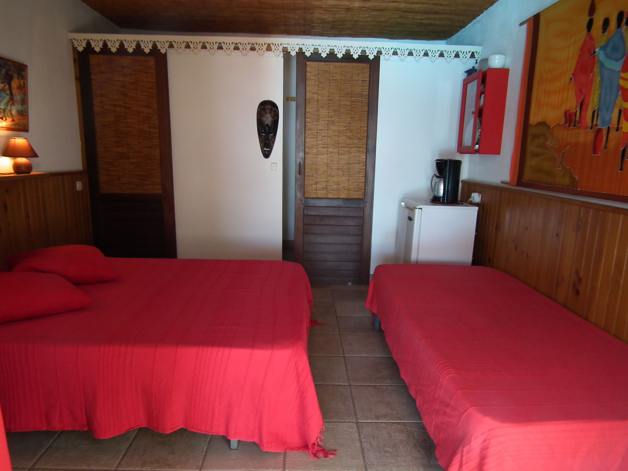 Chambre n°5 – lit avec literie rouge, kitchenette, peinture murale décorative