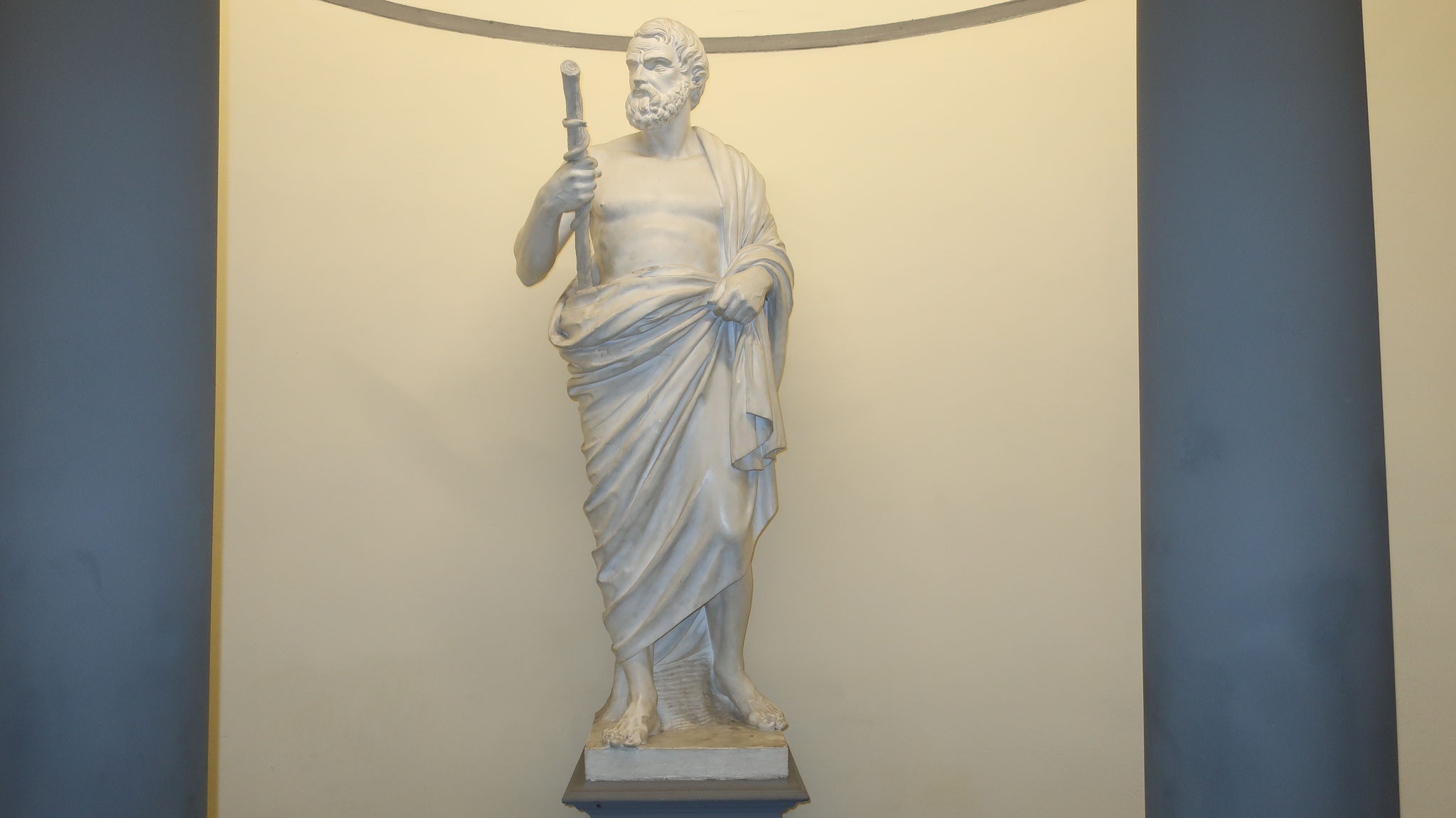 The statue of the healing deity Asclepius inside the shop. He has a staff entwined with a serpent, a symbol of medicine.