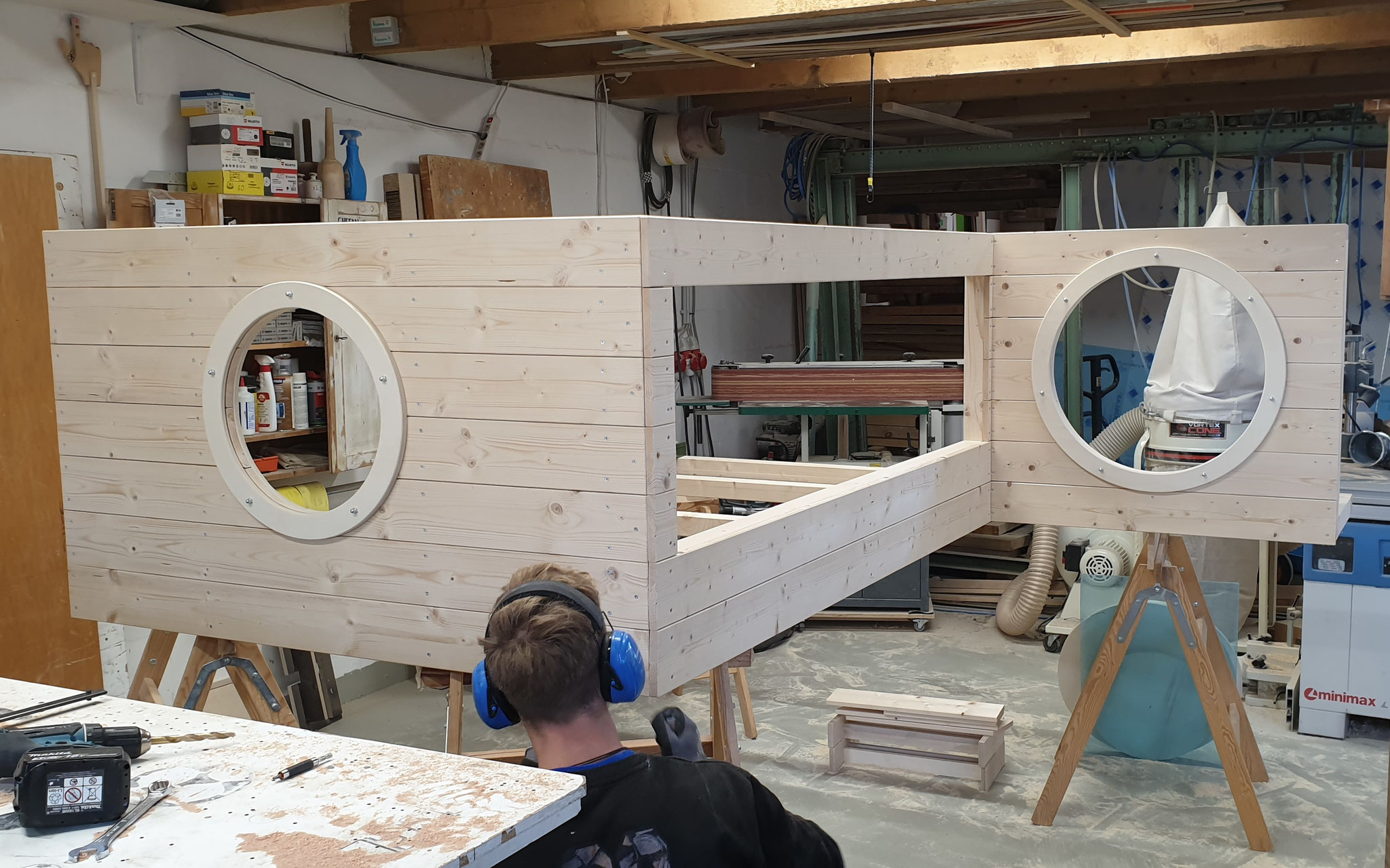 Bild von Prozess in der Werkstatt, großes Element, aus Massivholz mit runden und eckige Ausspahrungen, wird gebaut, steht auf einem Arbeitstisch