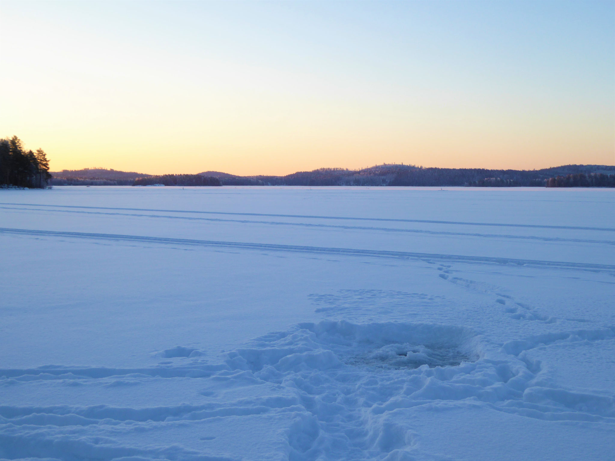 Ice fishing on the lake in front of log house and ...