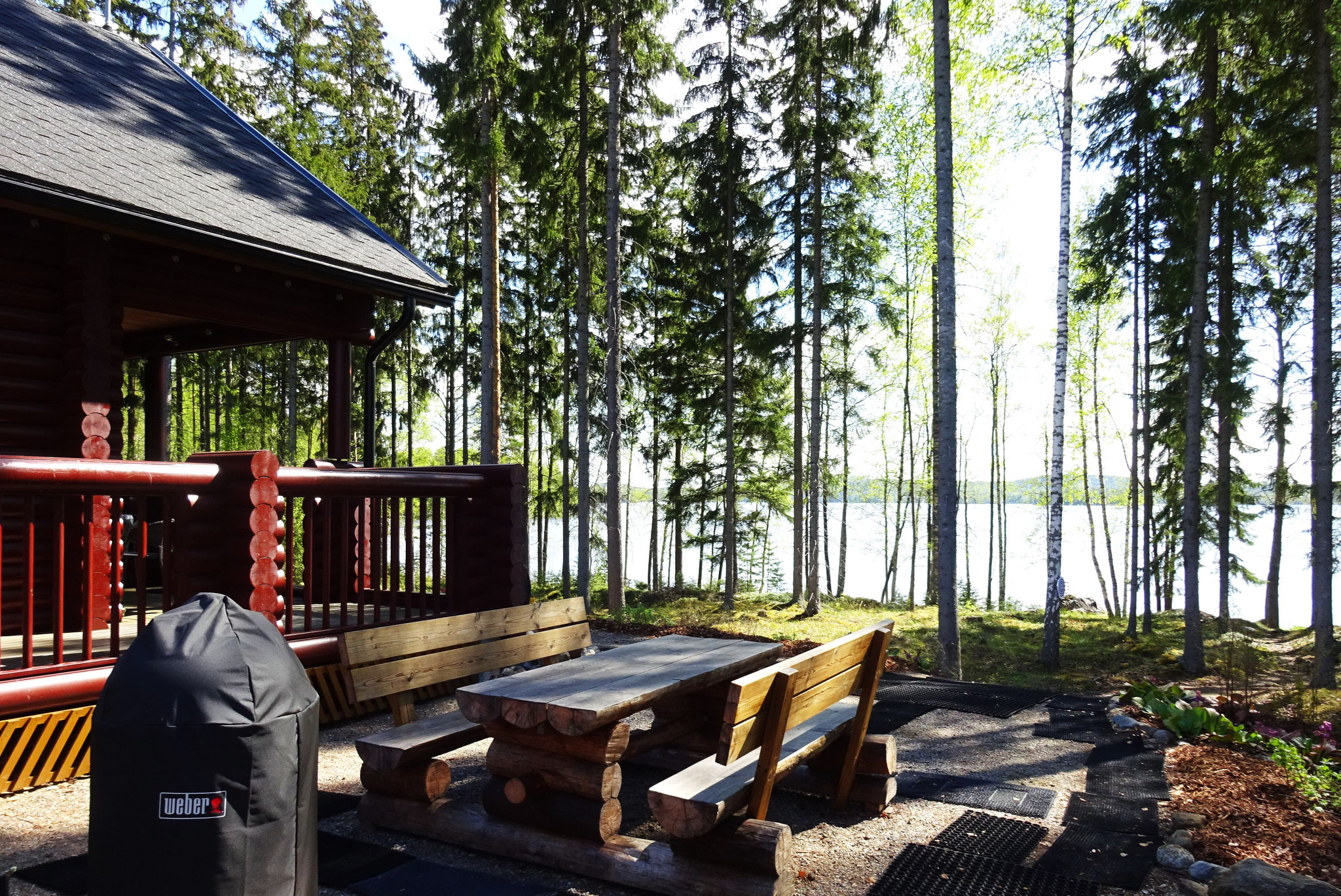 Rustikale Sitzgruppe Westseite zwischen Haus und Außensauna. Abendsonne und Blick auf den See beim Wellenrauschen. Kugelgrill und Weber Smoker