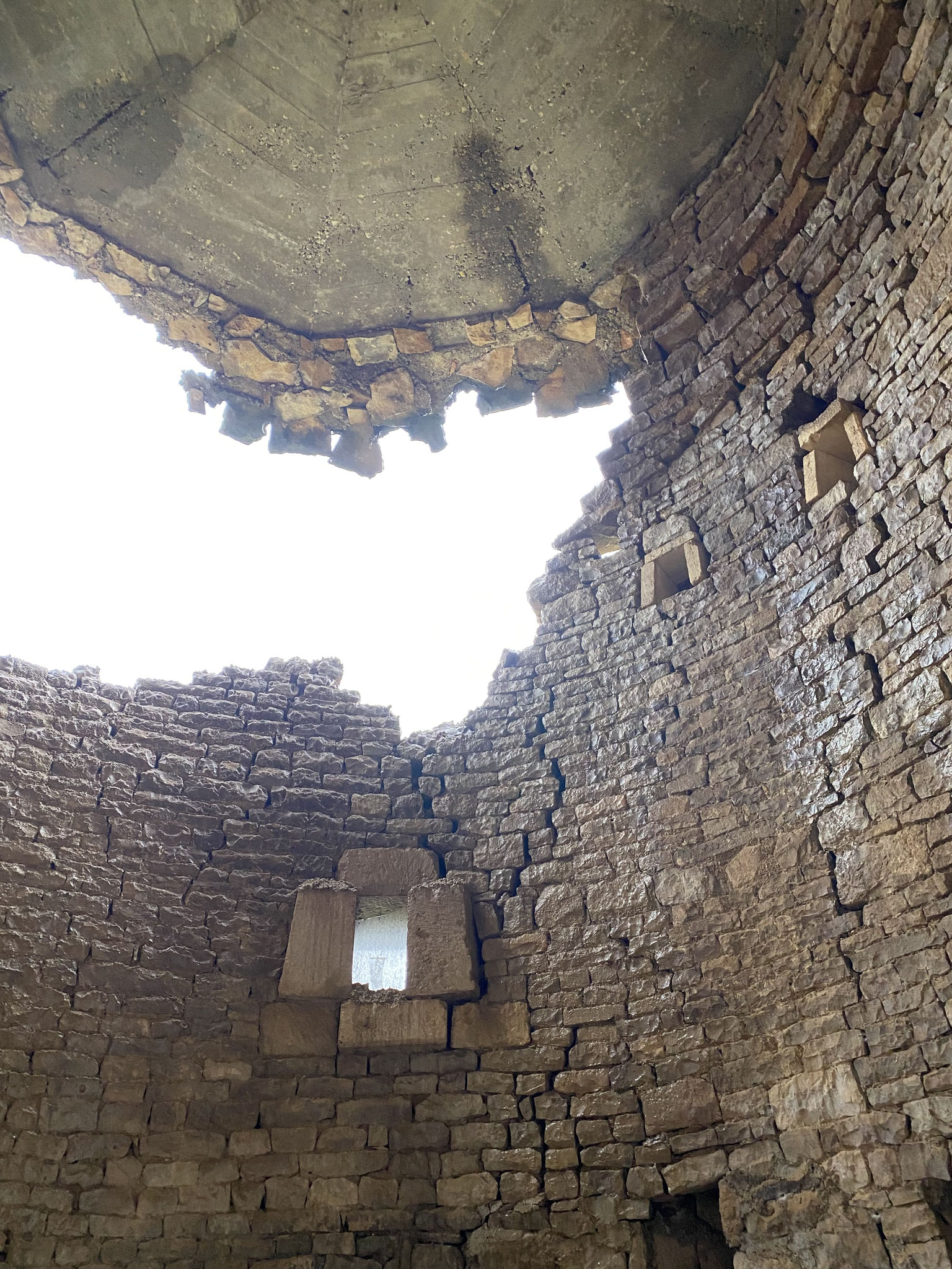    Vu de l'intérieur de la tour, trou béant laissant la lumière pénétrer et absence de support de la calotte en béton faisant office de toiture.