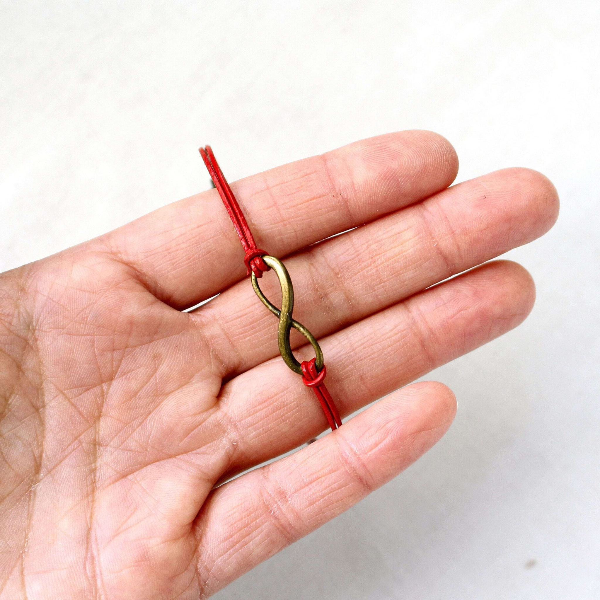 Handgemachtes Infinity‑Armband mit rotem Band in der Hand gehalten, präsentiert als modernes, symbolisches Schmuckstück für Geschenke.