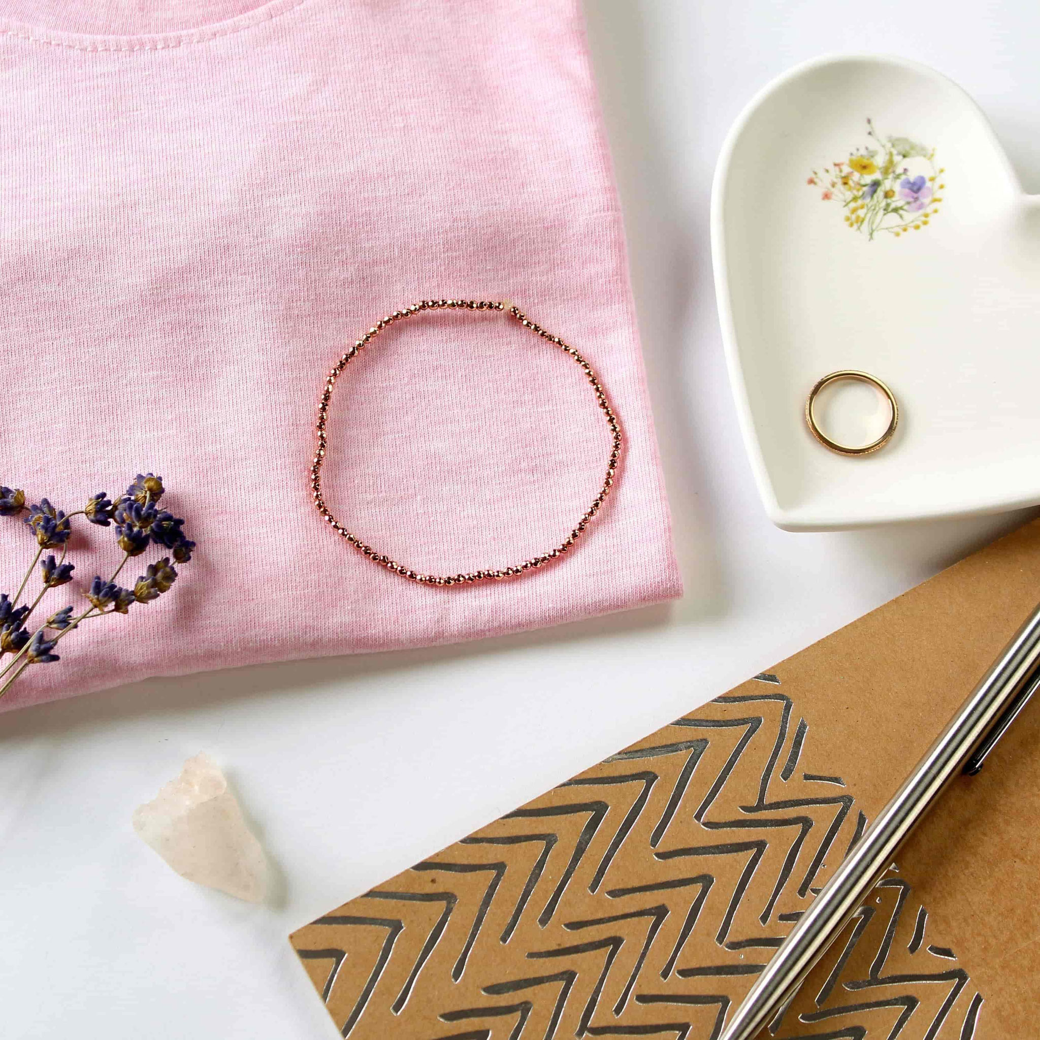 Roségold-Armband auf rosa Stoff mit Herzschale, Ring und Deko.