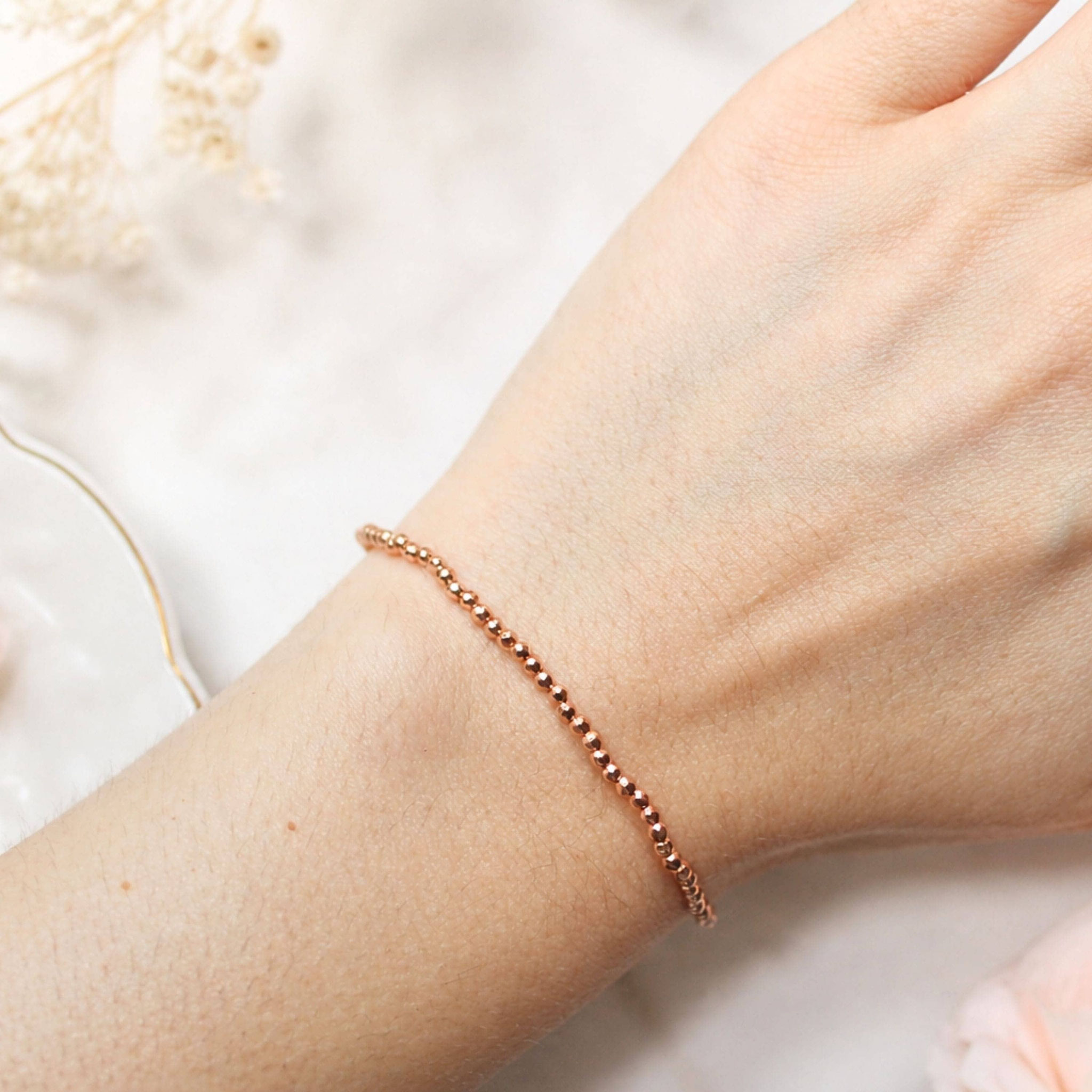 Roségold-Armband am Handgelenk, umgeben von weicher Deko.