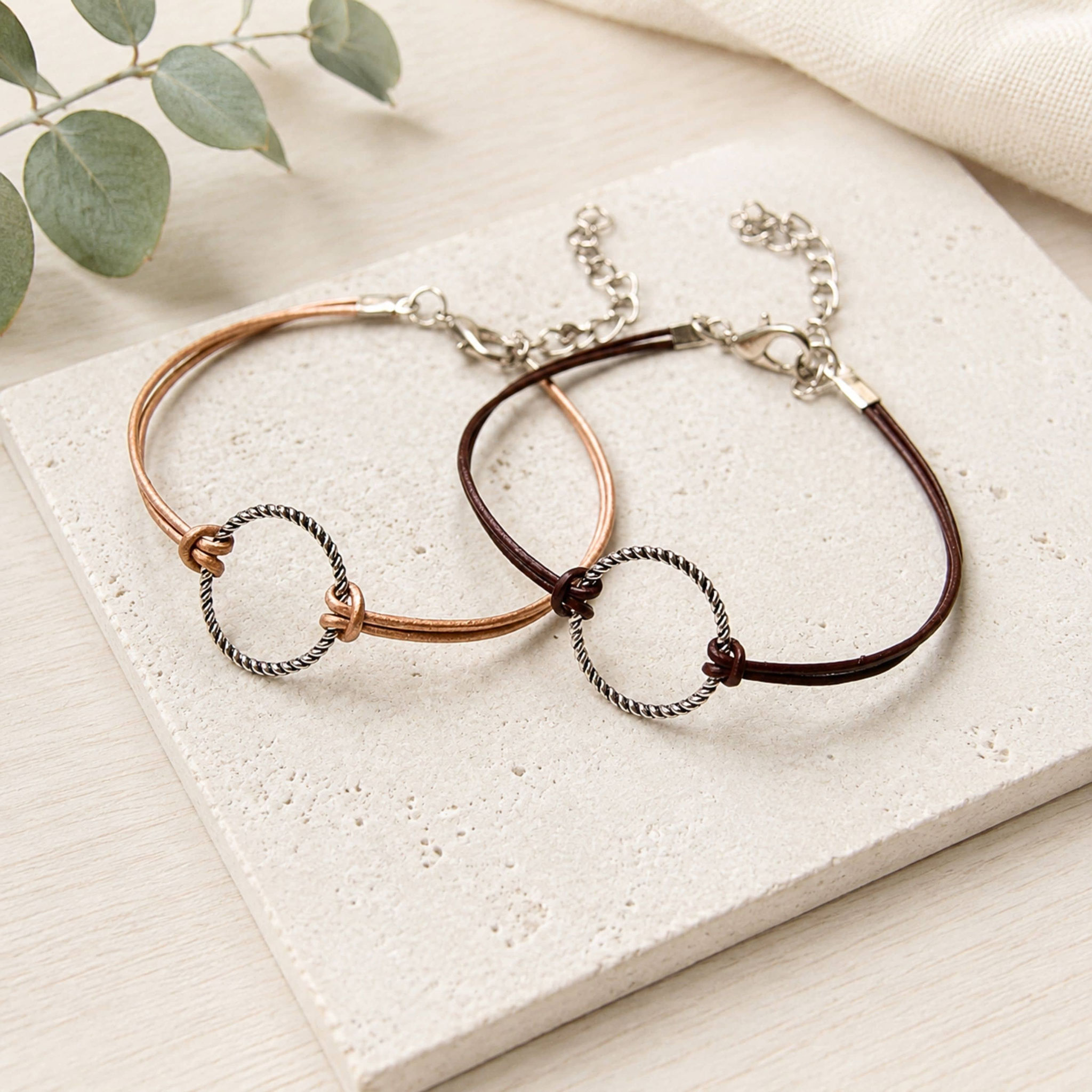 Zwei Lederarmbänder mit silbernem Ringelement in Braun und Dunkelbraun.