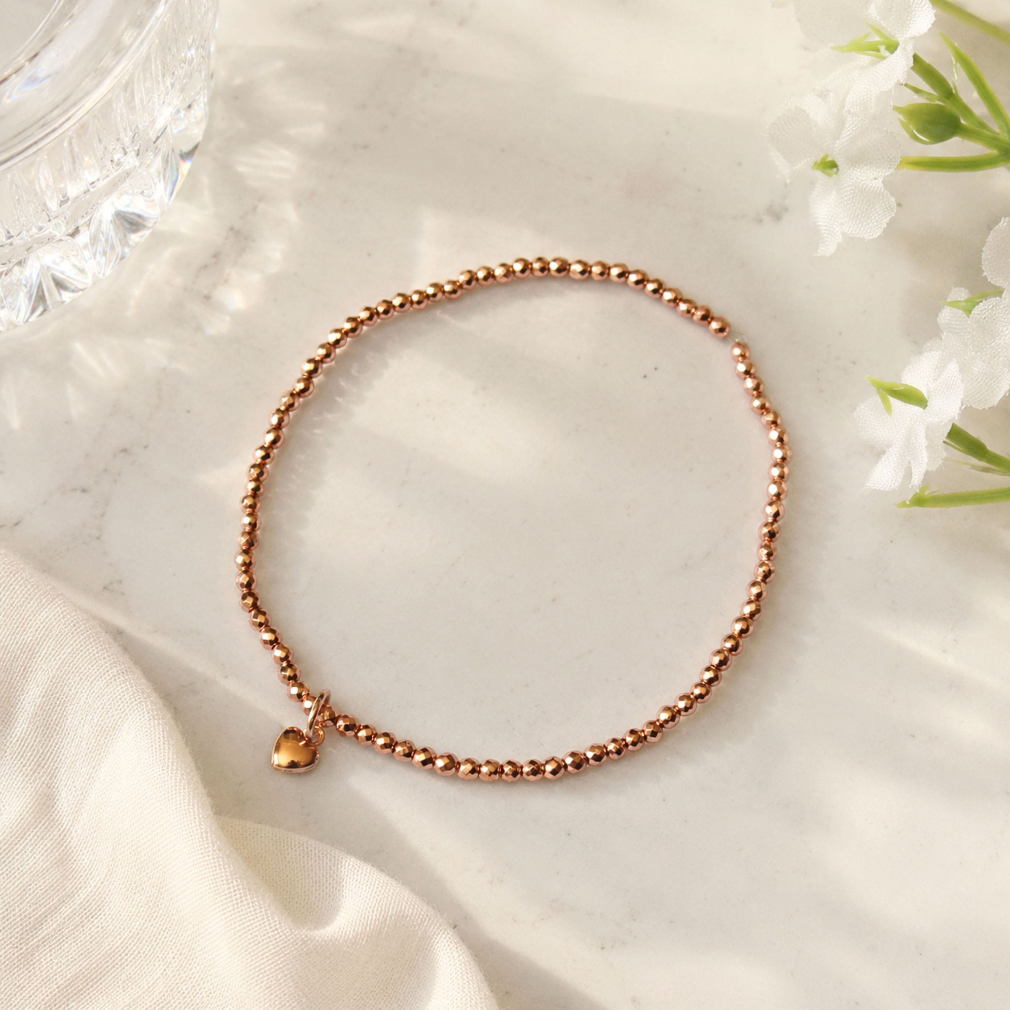 Roségoldenes Perlenarmband mit Herzanhänger auf hellem Marmorfond, dekorativ arrangiert.