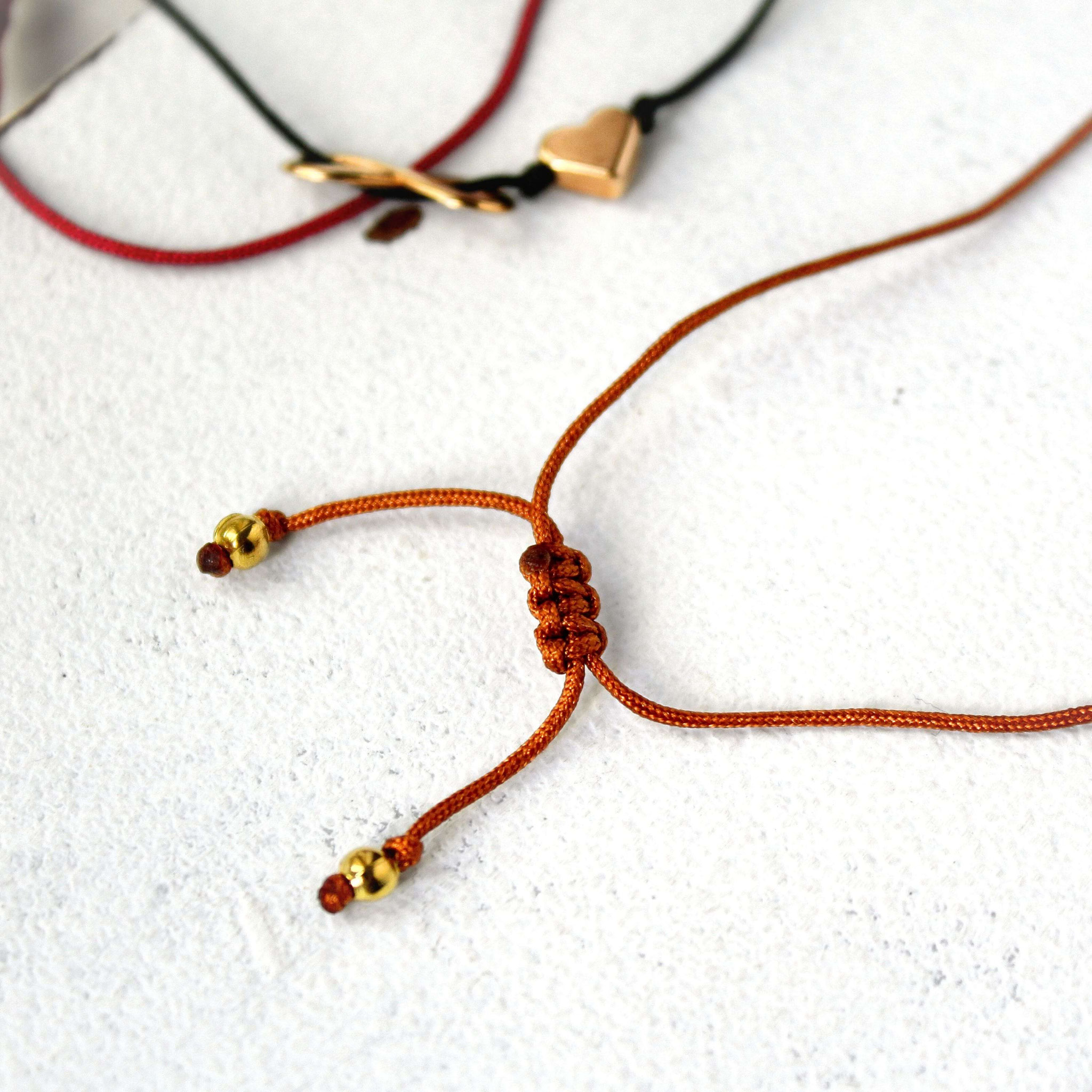 Nahaufnahme dreier Makramee‑Armbänder aus farbigen Bändern mit Herz‑ und Infinity‑Details als handgemachter Schmuck.