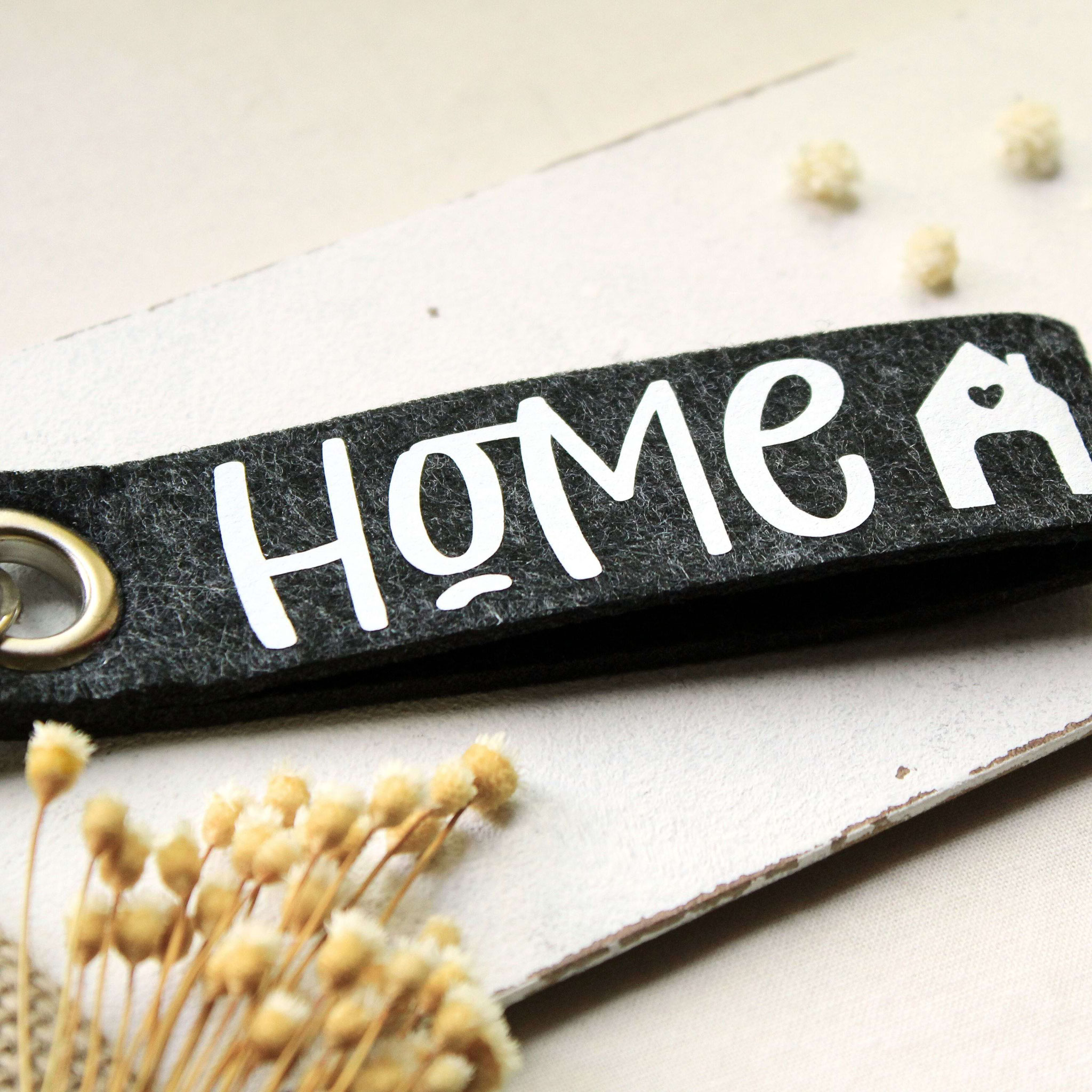 Schwarzer Filz-Schlüsselanhänger mit „HOME“-Print und Herzhaus-Symbol – dekoratives Accessoire für Schlüssel oder Taschen.