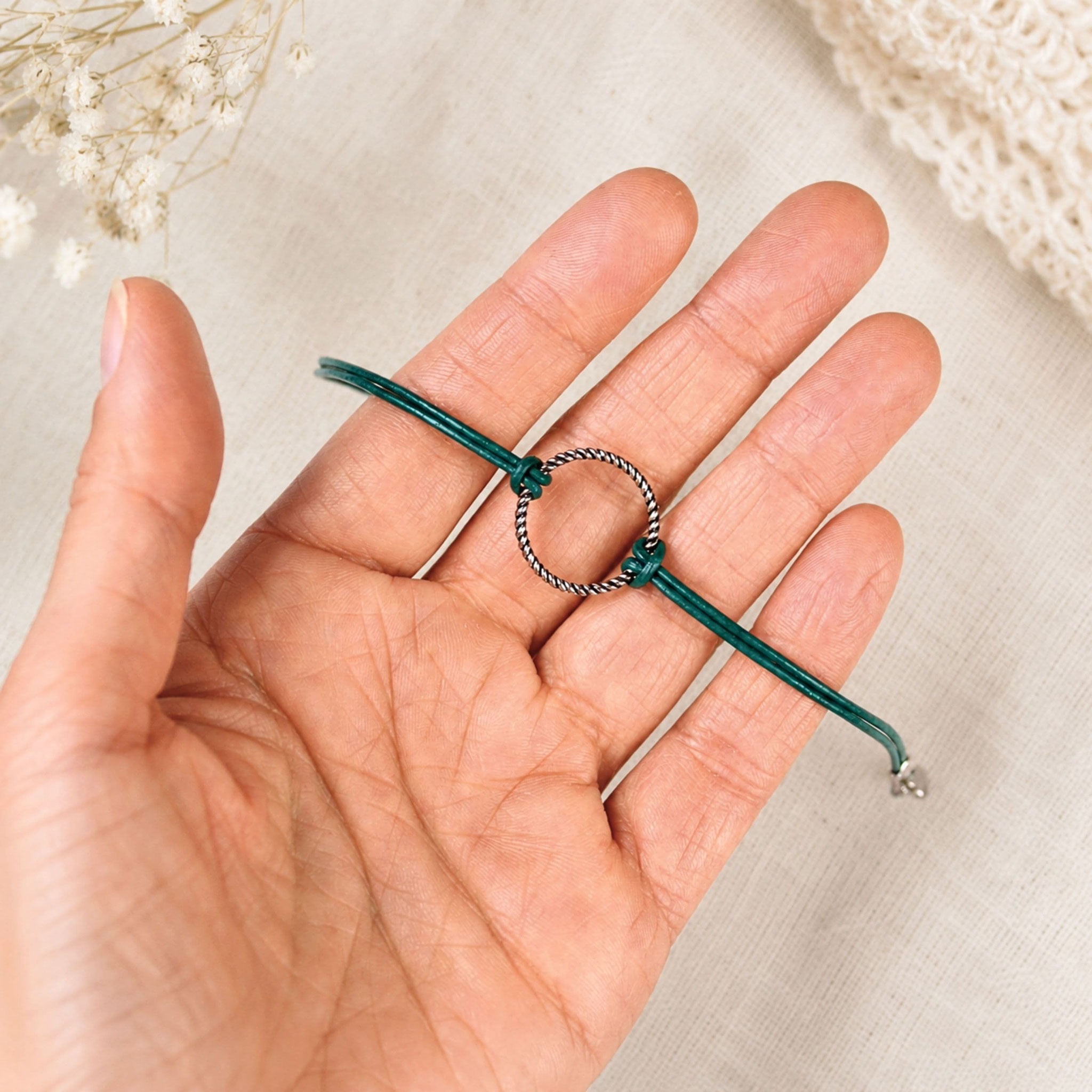 Detailaufnahme eines grünen Lederarmbands mit silbernem Ringelement in der Hand.
