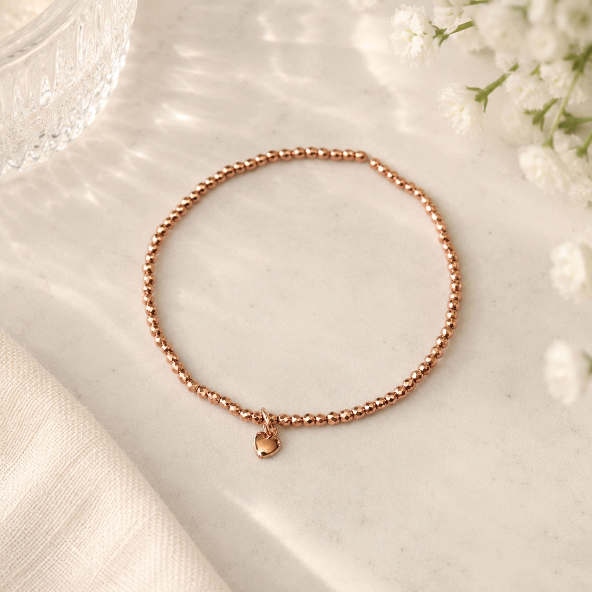Roségoldenes Perlenarmband mit Herzanhänger auf hellem Untergrund.