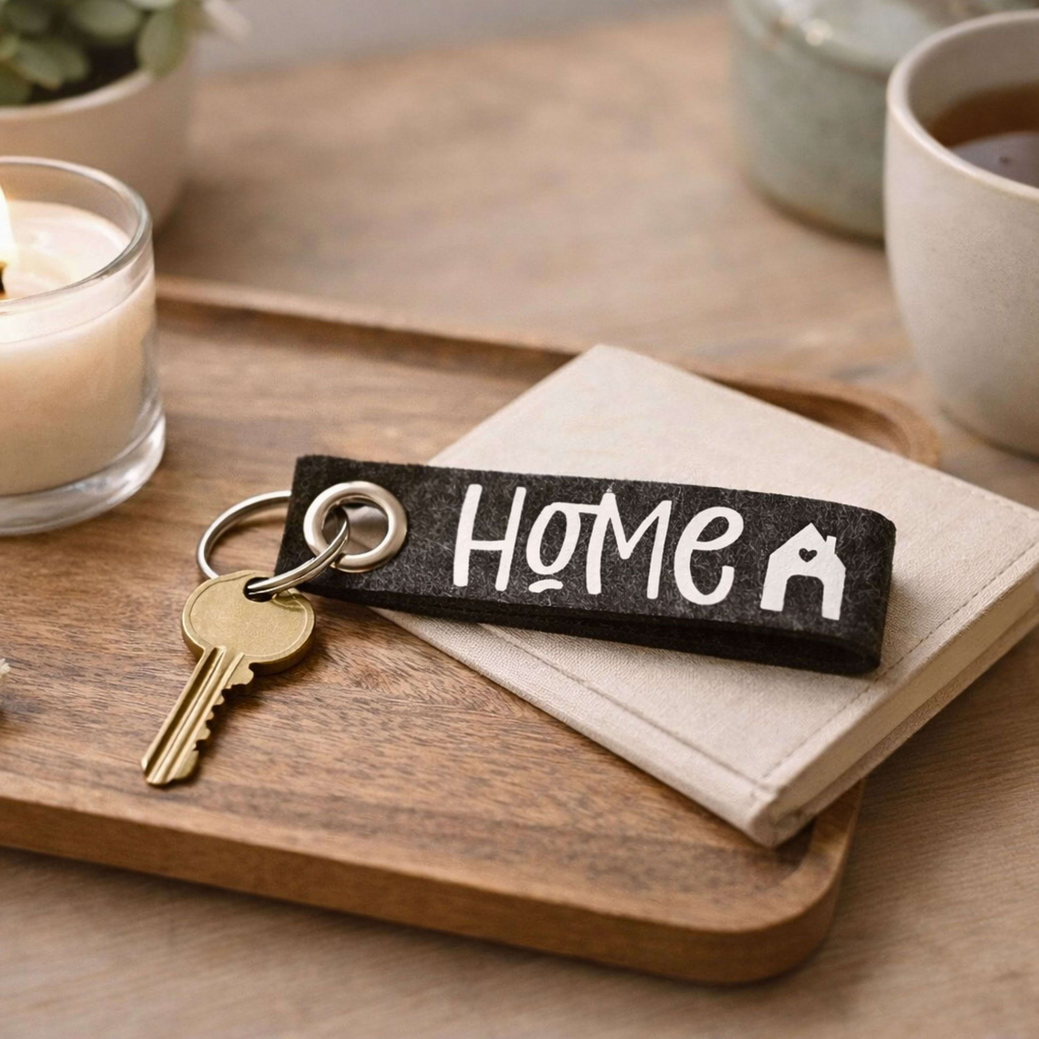 Holztablett mit Tee, Kerze, Notizbuch und „Home“-Schlüsselanhänger – gemütliches Stillleben für Zuhause und Entspannung.