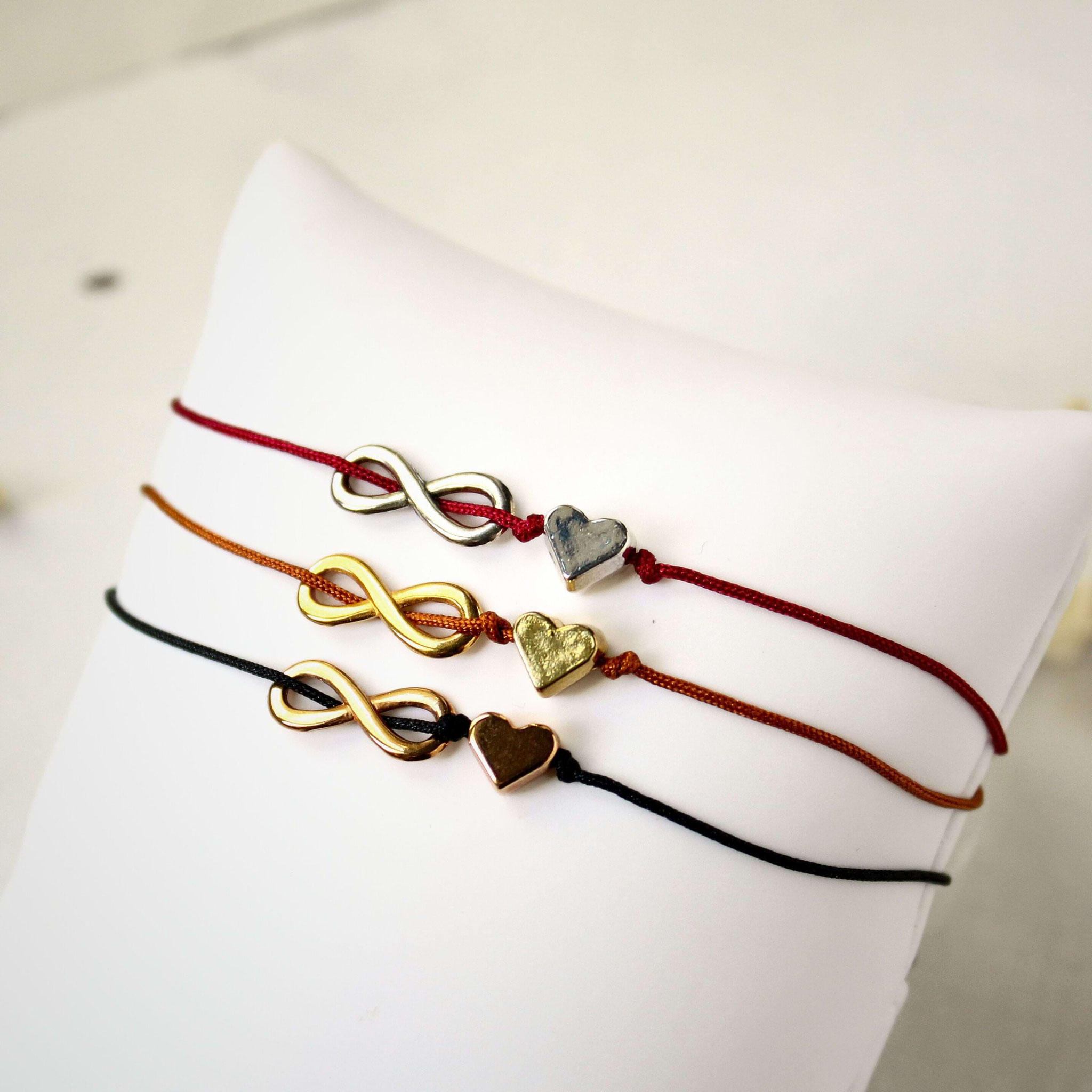 Ruhige Produktaufnahme von drei Makramee‑Armbändern mit Infinity‑ und Herzanhängern als handgemachter Geschenk‑ und Freundschaftsschmuck.