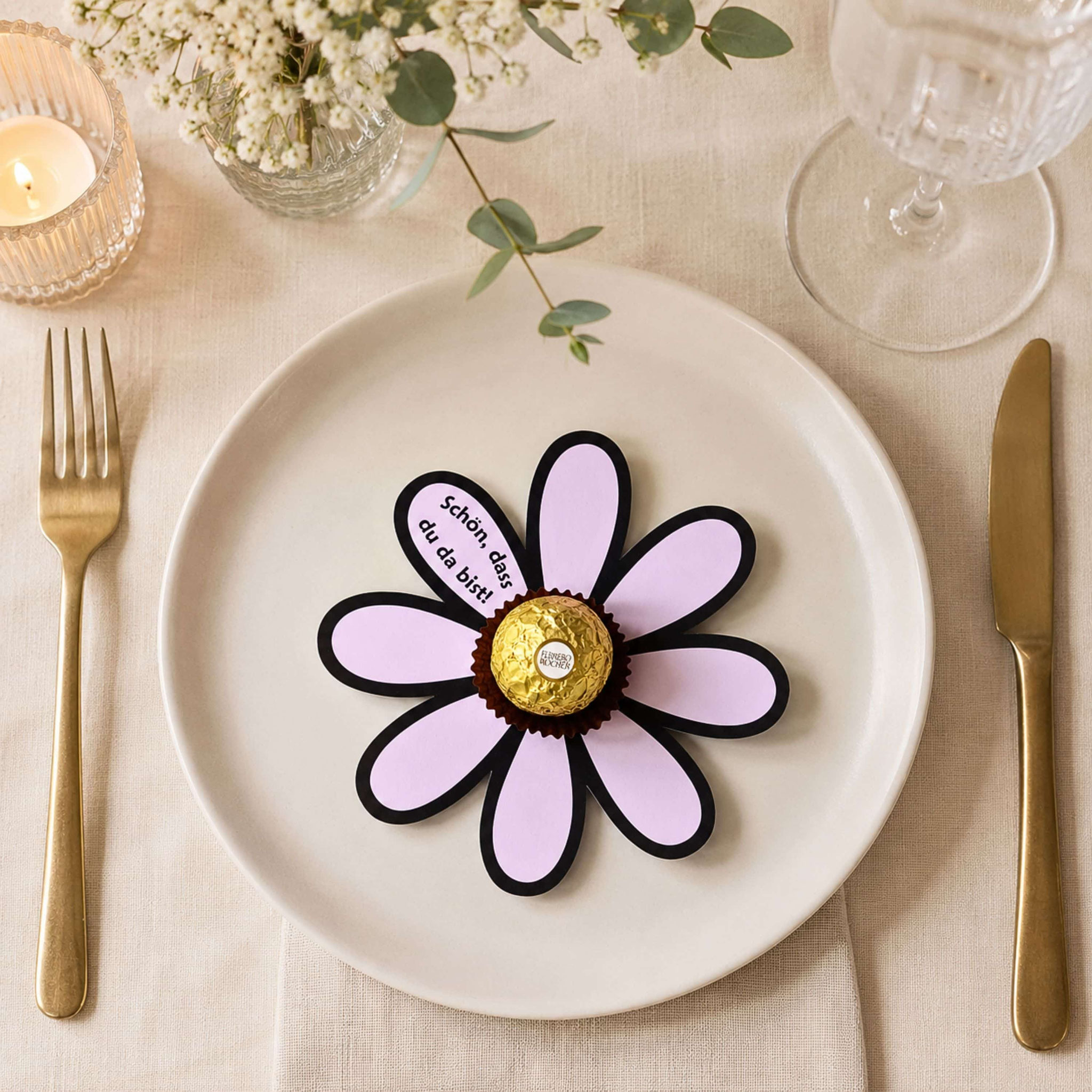 Papierblume mit Ferrero Rocher und „Schön, dass du da bist!“ als elegantes Gastgeschenk auf gedecktem Tisch.