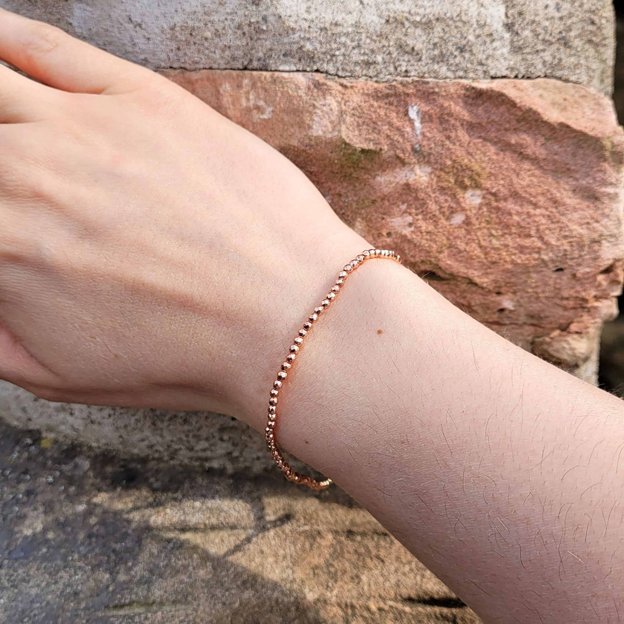 Roségold-Armband am Handgelenk vor Naturstein-Hintergrund.