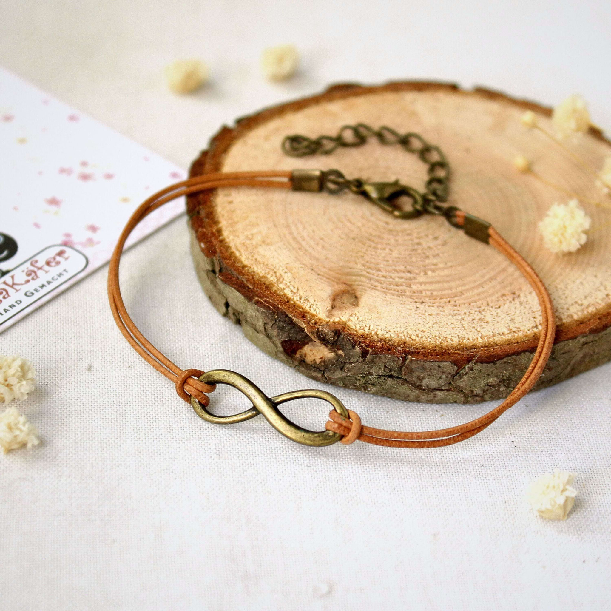 Handgemachtes Lederarmband mit bronzefarbenem Infinity-Symbol auf Holzuntergrund, ideal als personalisiertes Geschenk.