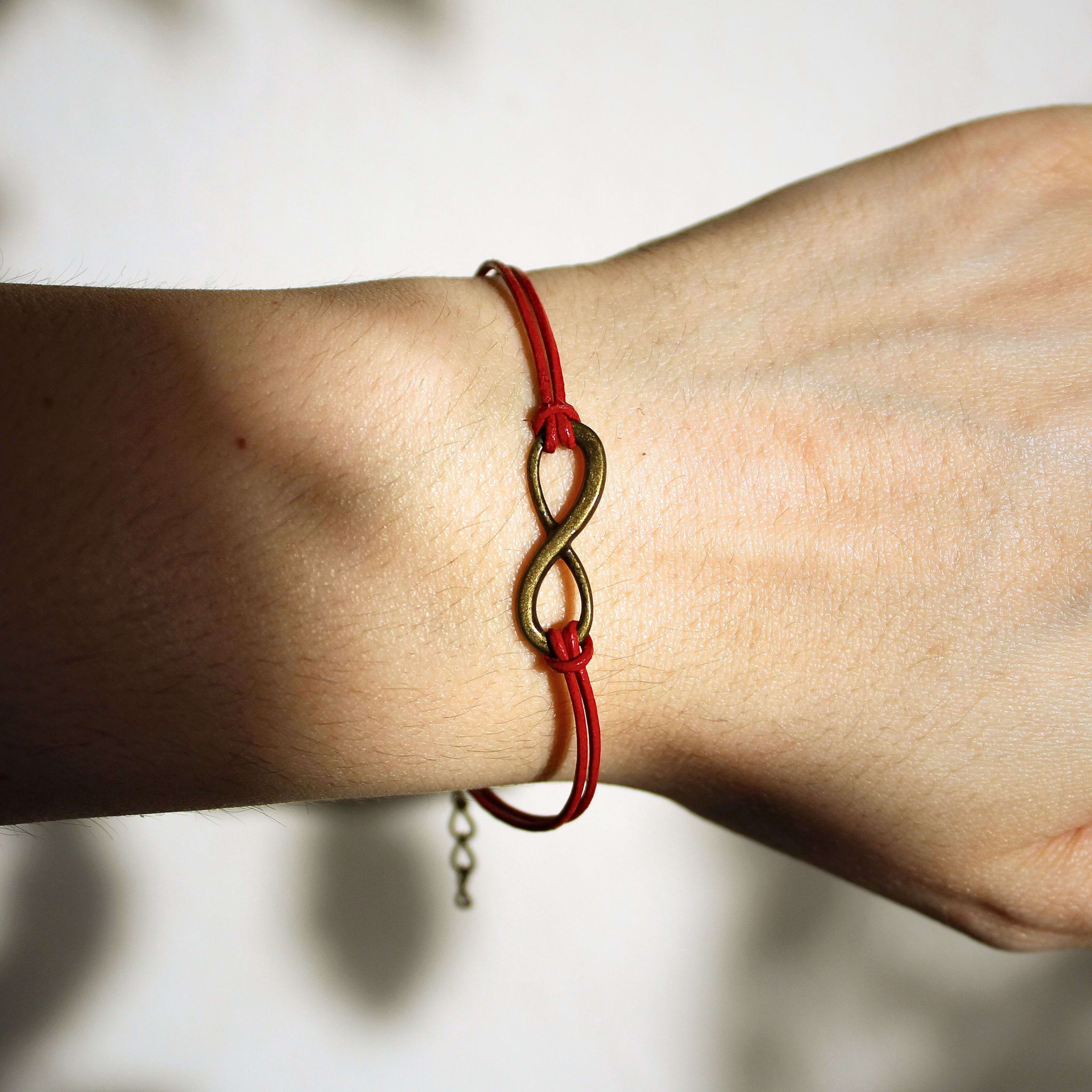 Handgemachtes Infinity‑Armband mit rotem Band am Handgelenk getragen, gezeigt als modernes, symbolisches Schmuckstück für persönliche Geschenke.