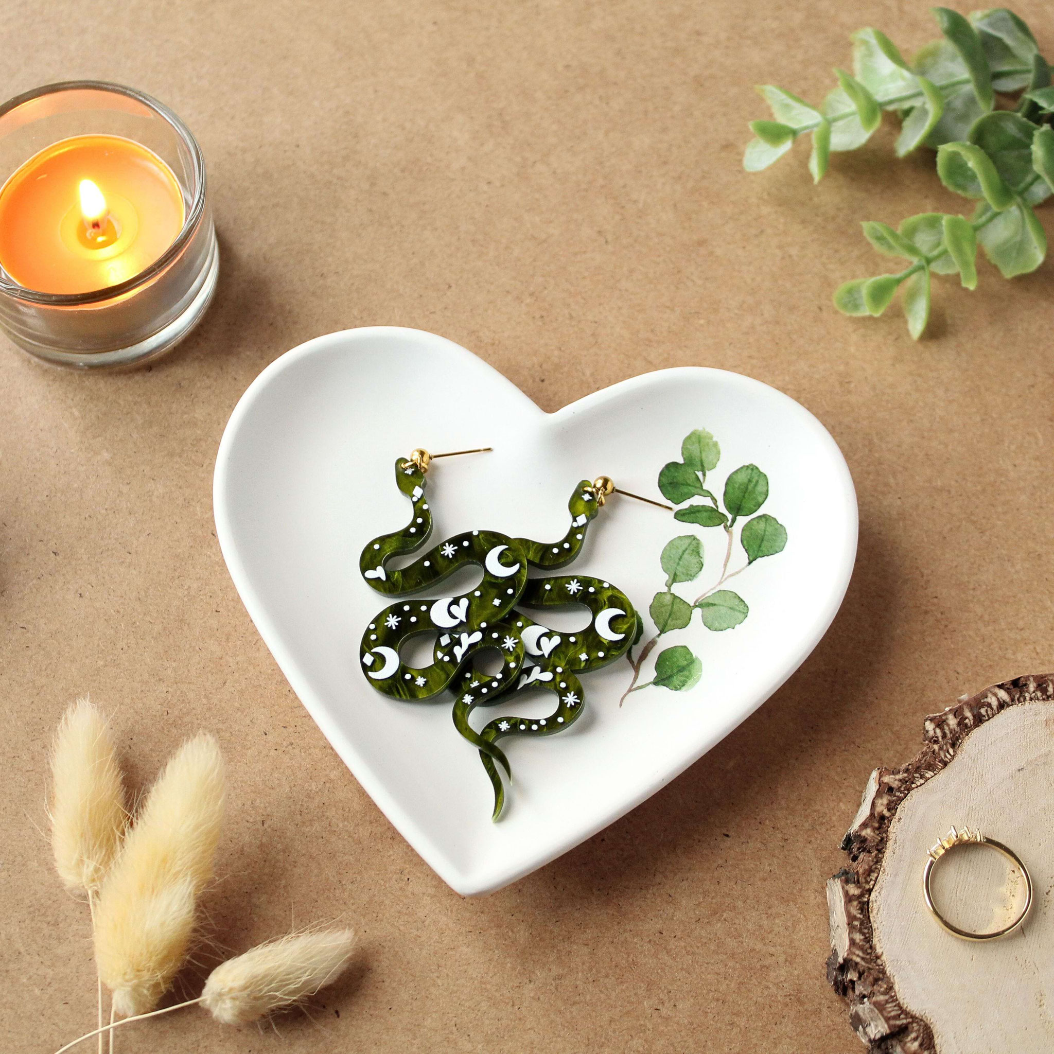 Herzschale mit grünen Schlangenohrringen, umgeben von Deko.