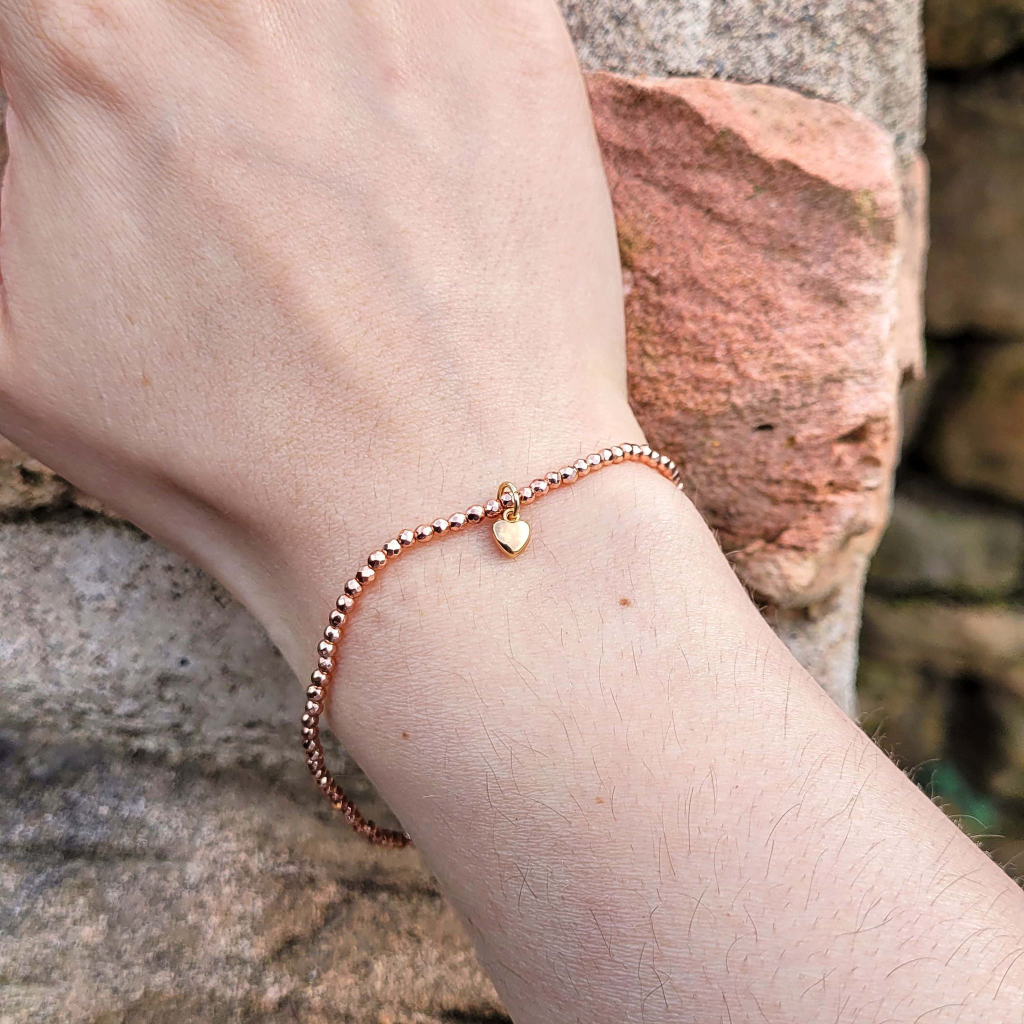 Roségoldenes Perlenarmband mit Herzanhänger am Handgelenk.