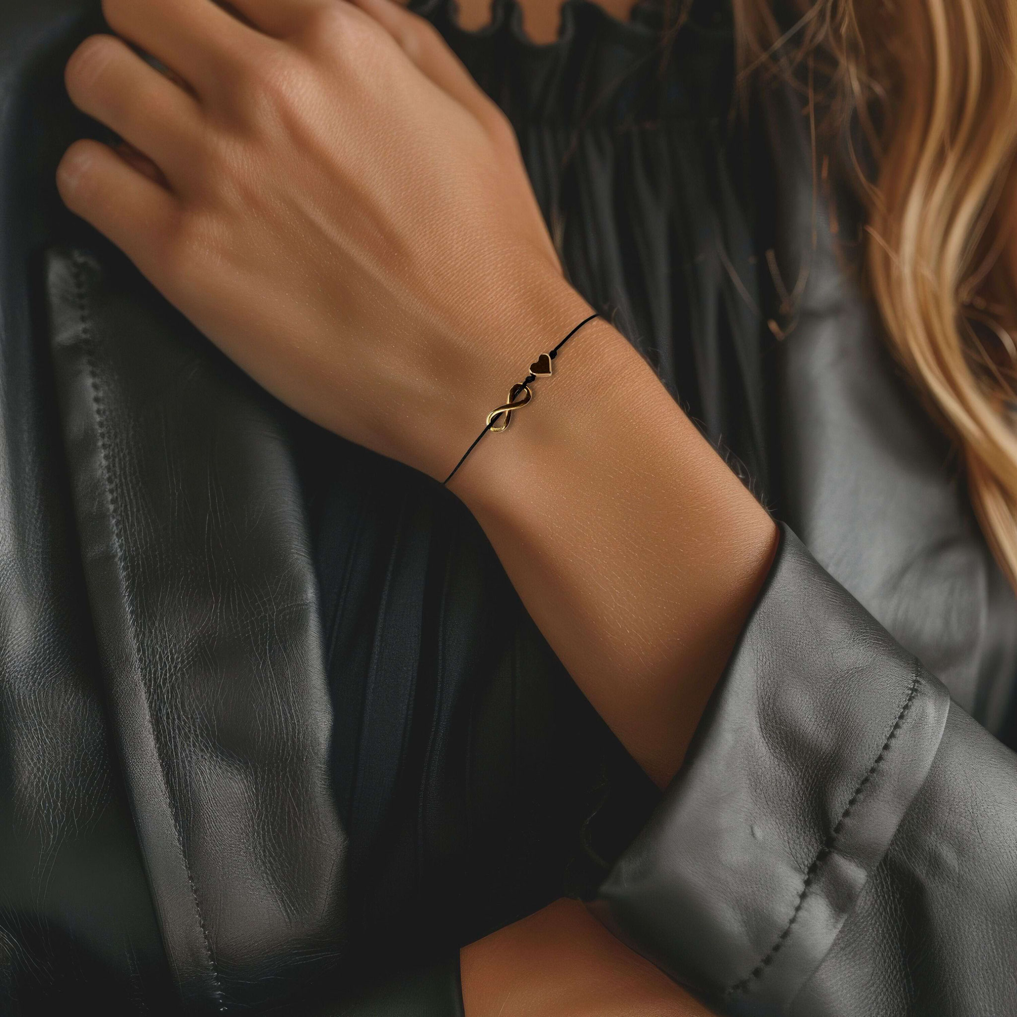 Ruhige Nahaufnahme eines schwarzen Makramee‑Armbands mit goldenem Infinity‑Herz‑Anhänger als eleganter handgemachter Schmuck.