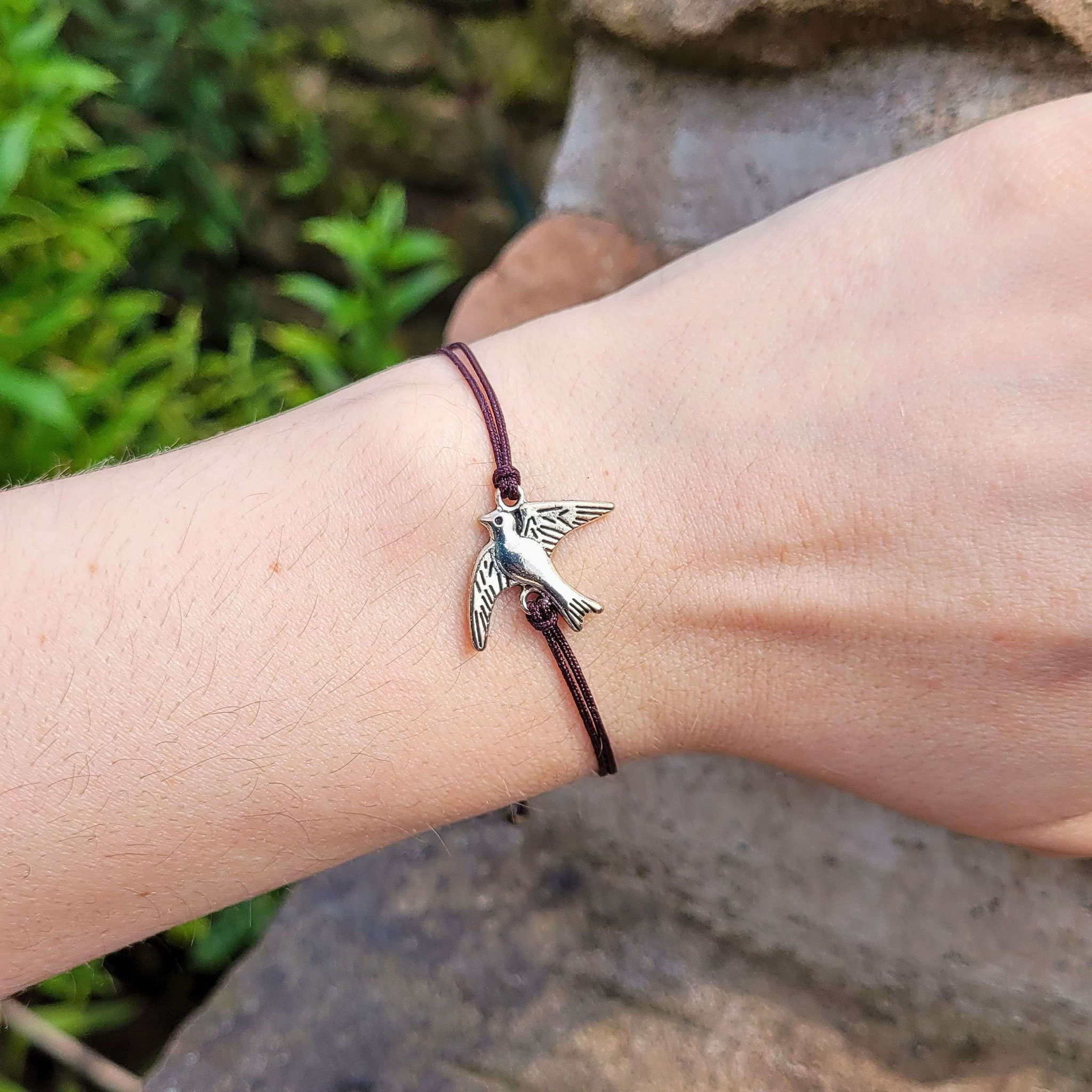 Makramee‑Armband mit Vogelanhänger am Handgelenk.