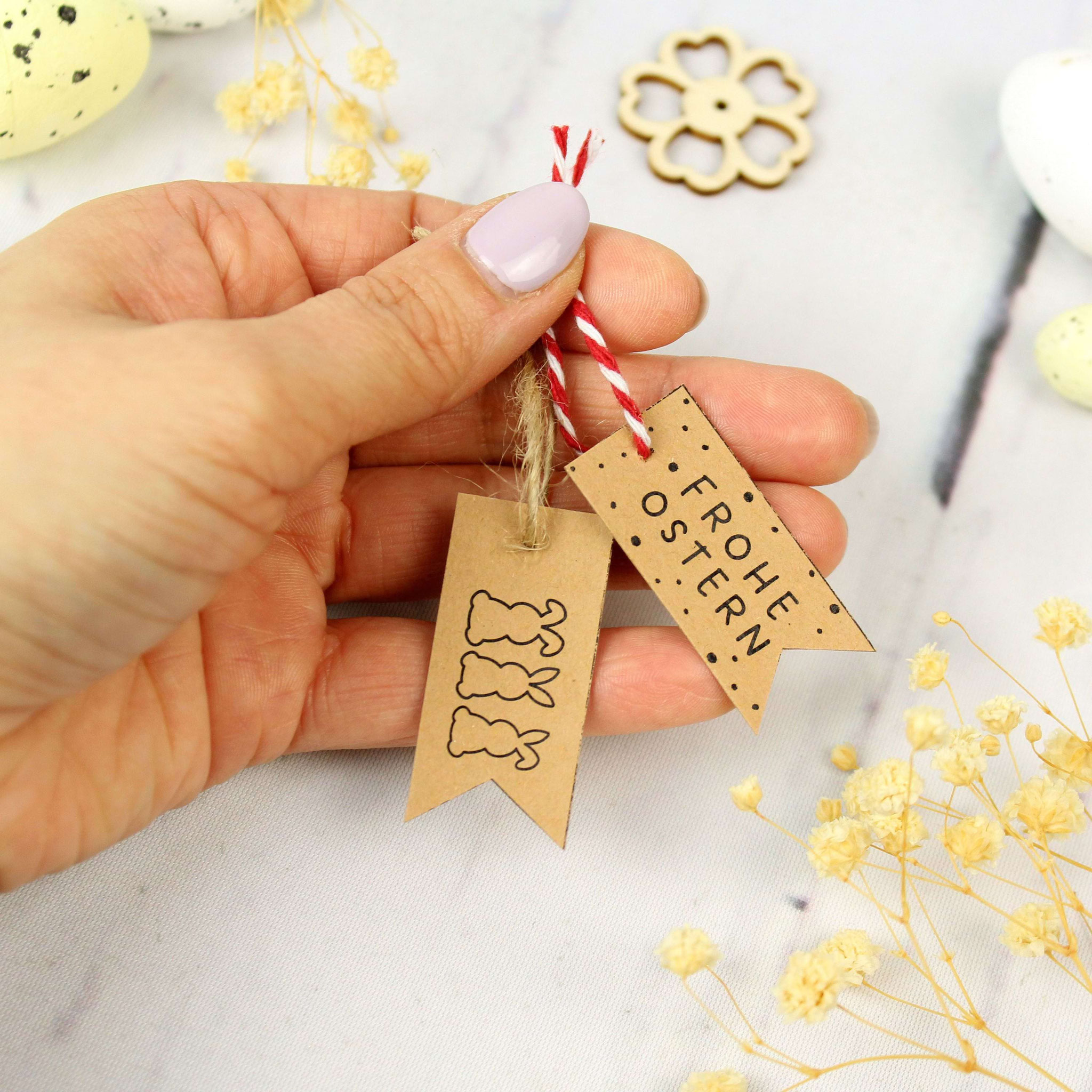 Oster-Geschenkanhänger aus Kraftpapier mit Hasen und „Frohe Ostern“, dekoriert mit Eiern und Frühlingselementen.