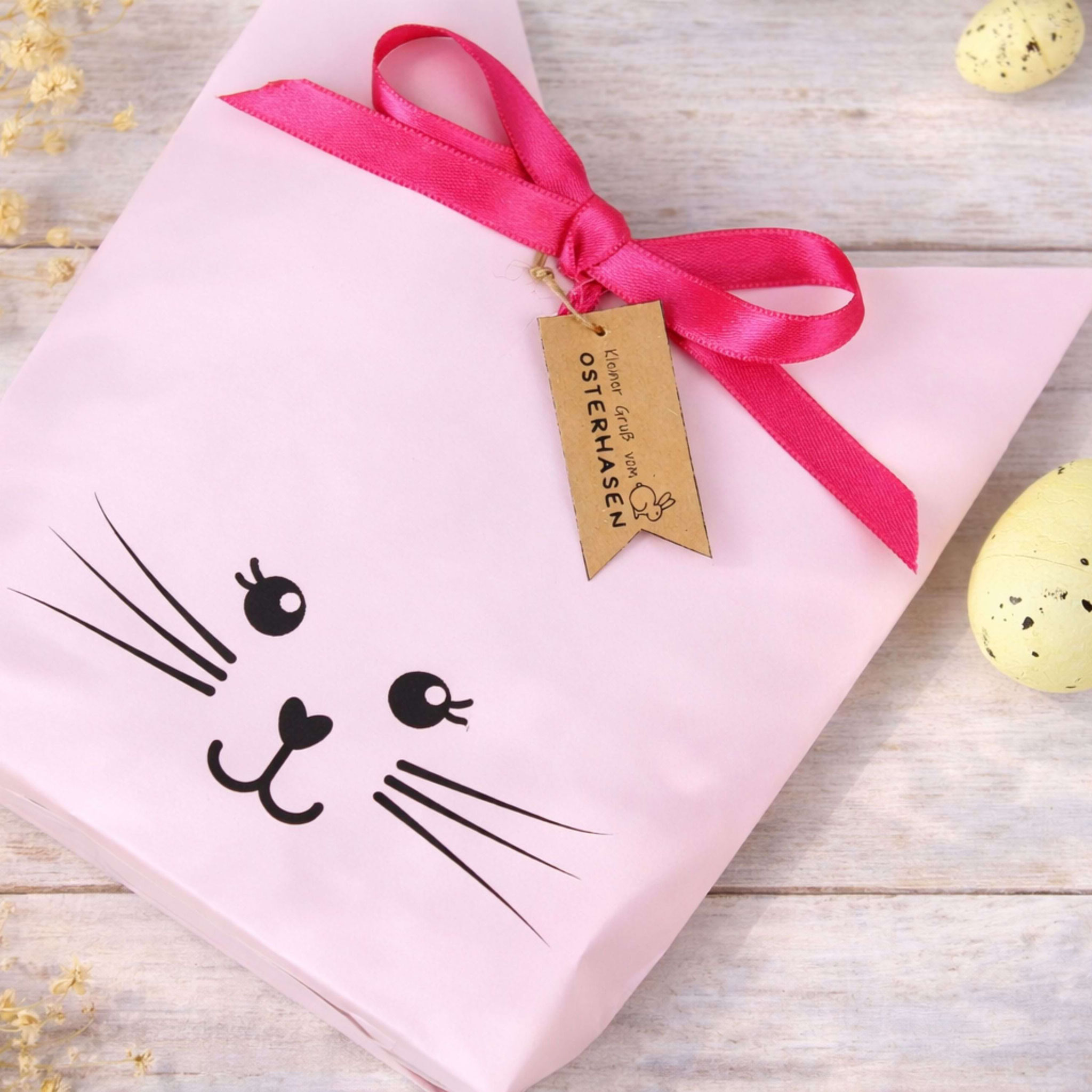 Rosa Oster-Geschenktüte im Hasendesign mit Anhänger ‚Gruß vom Osterhasen‘, dekorativ arrangiert als DIY‑Ostergeschenkidee.