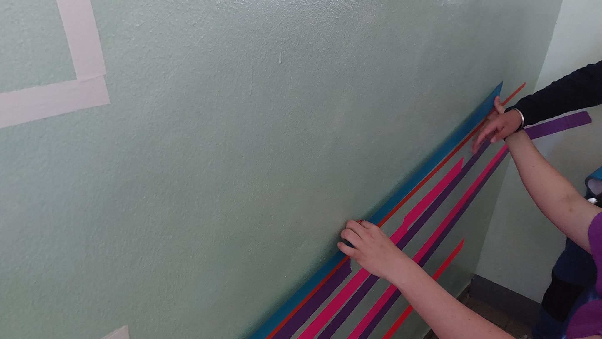 Neonfarbene Klebestreifen werden an eine Wand geklebt.