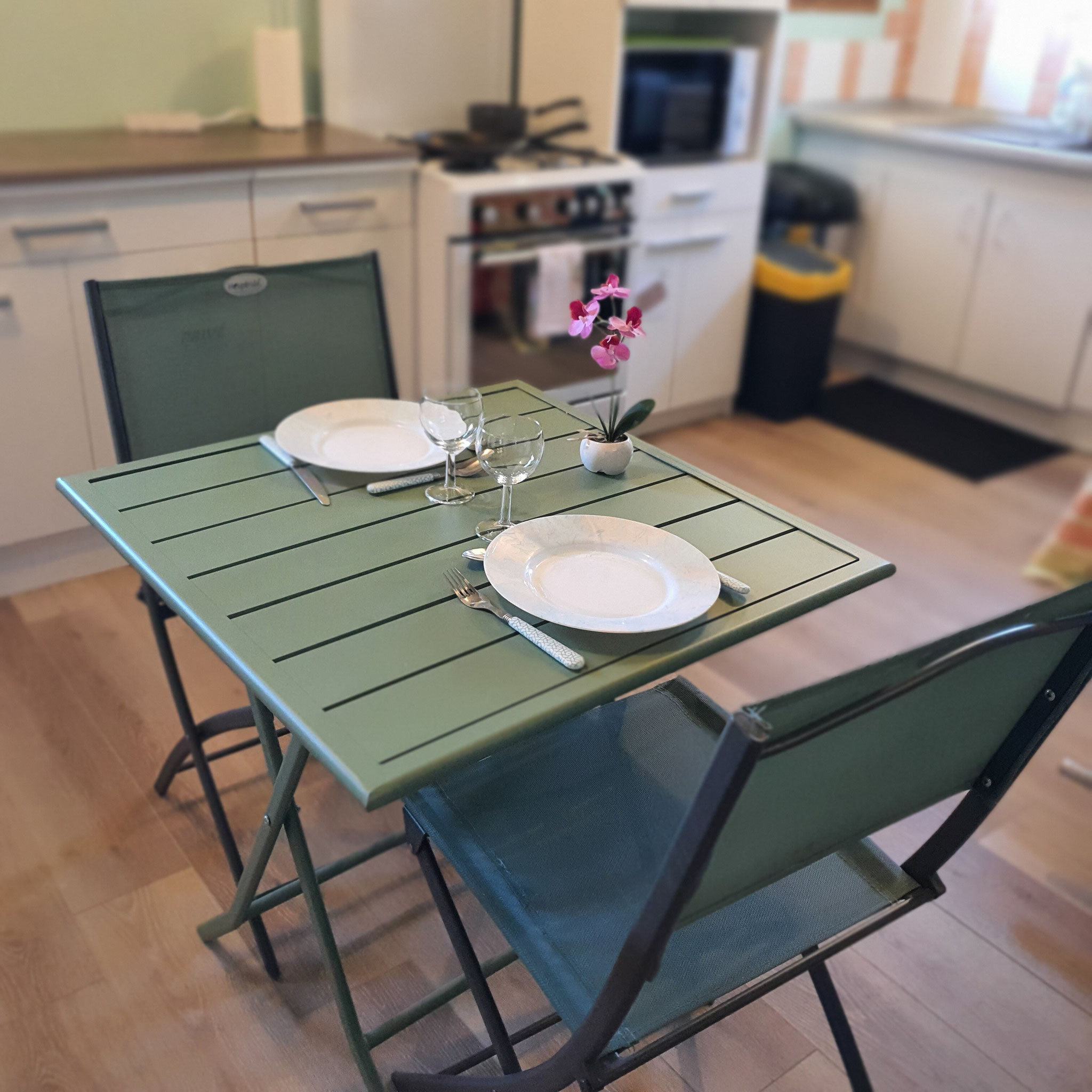 Table mise avec assiettes et couverts et deux chaises avec meubles en arrière plan