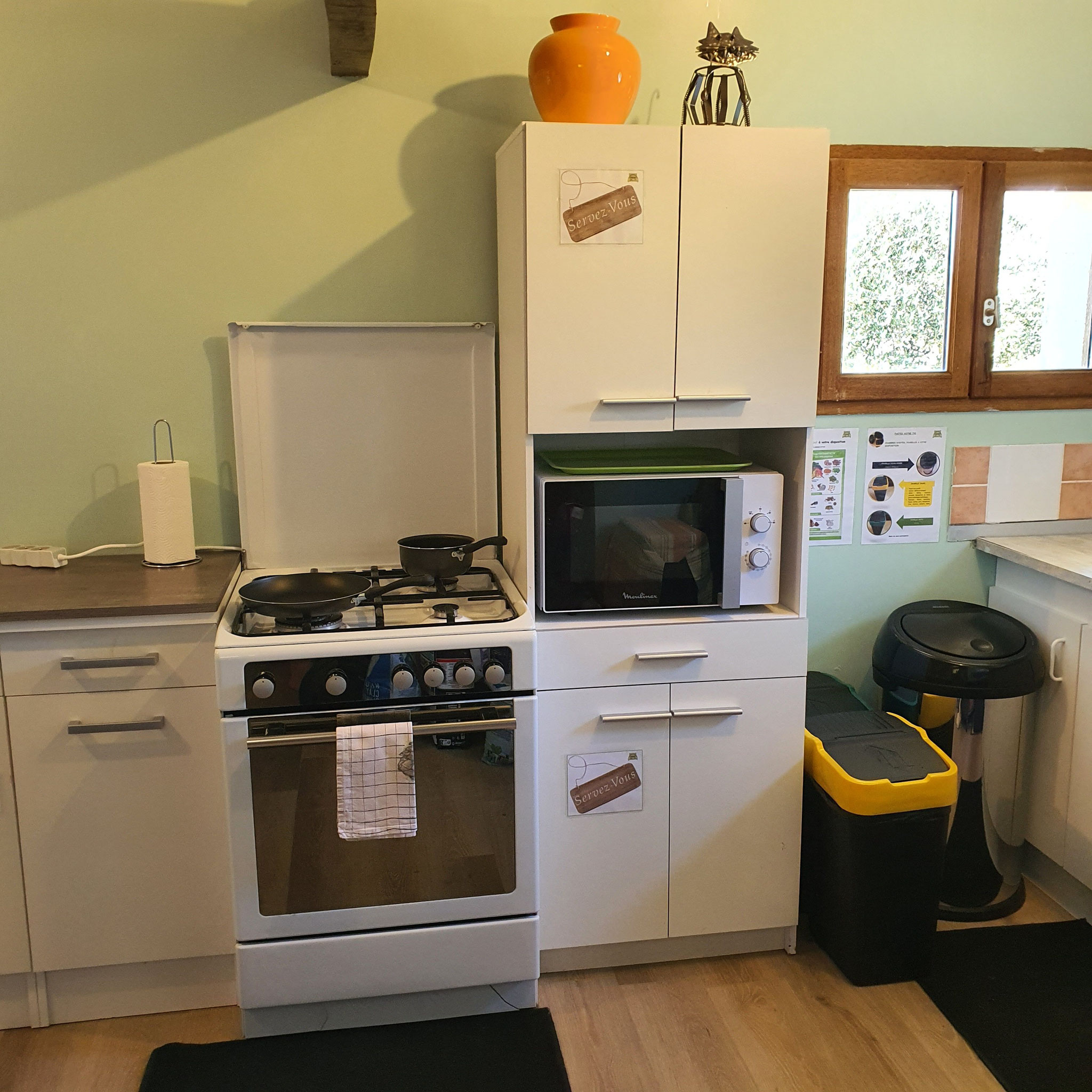 Coin cuisine lumineux avec cuisinière, meuble avec micro-ondes avec une fenêtre