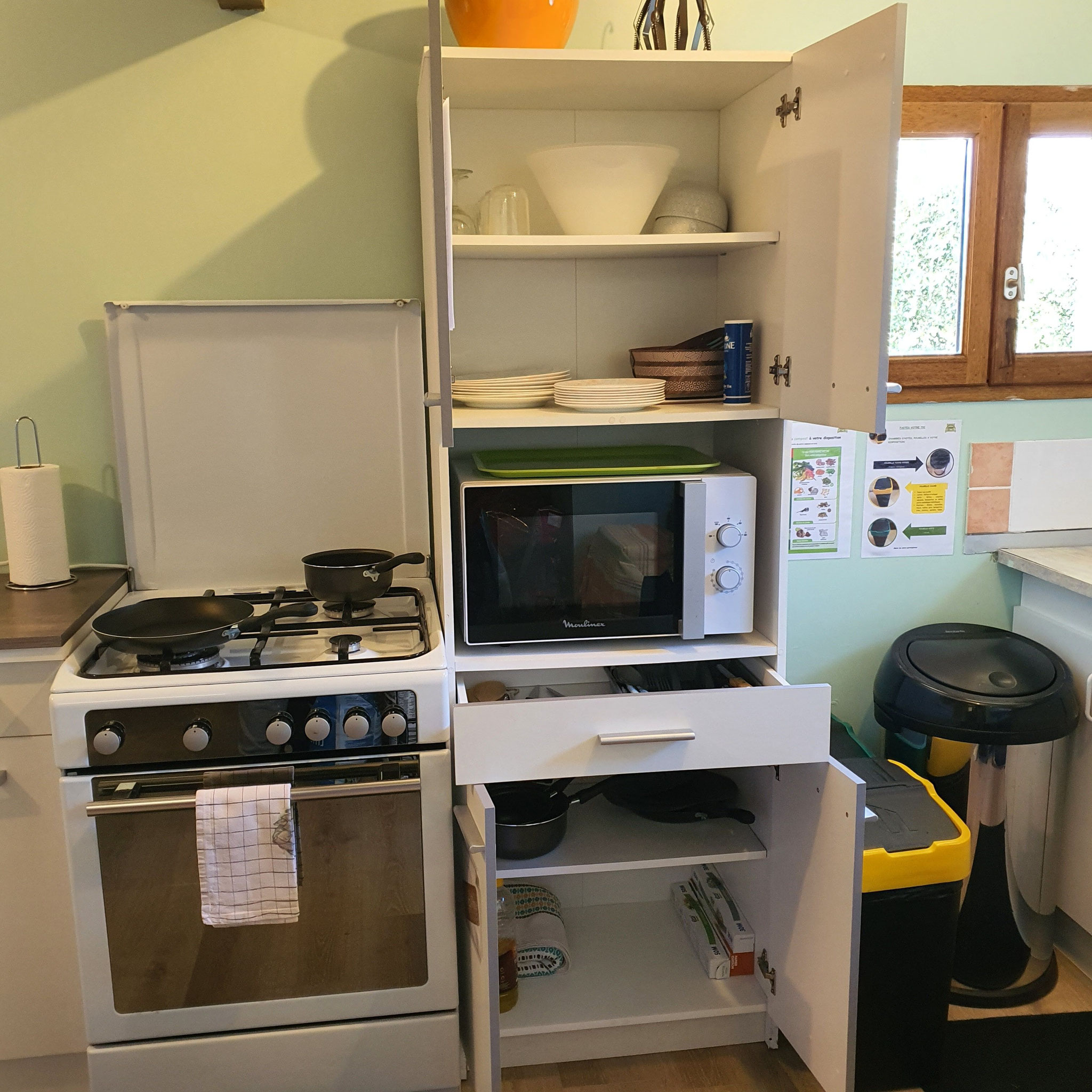 Coin cuisine lumineux avec cuisinière, meuble avec micro-ondes avec une fenêtre 