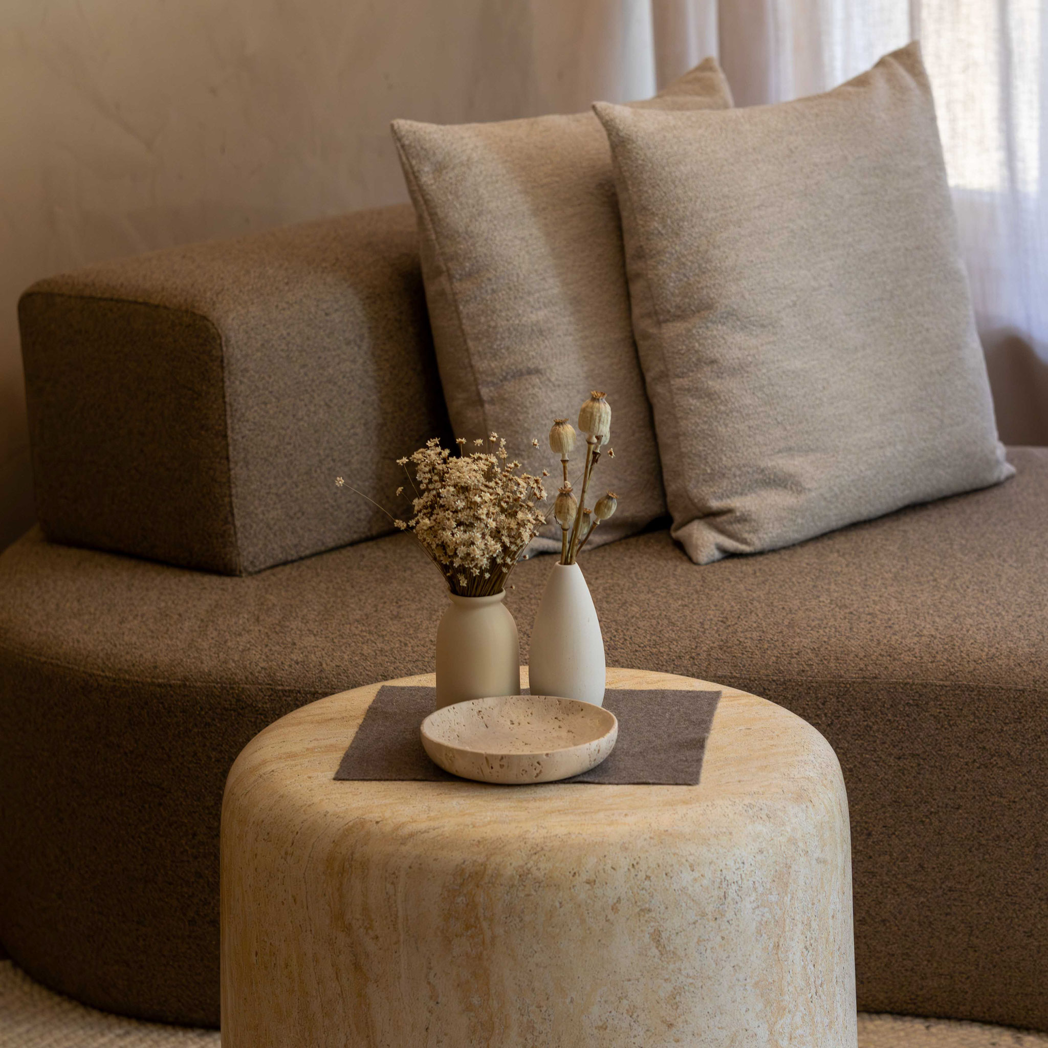 Gemütlicher Wohnbereich einer Suite im Boutiquehotel PETRUS in Reischach-Bruneck: Ein heller, runder Steintisch mit zwei kleinen Vasen und einer dekorativen Schale steht vor einem beigefarbenen Sofa mit großen Kissen und schafft eine ruhige, wohnliche Atm