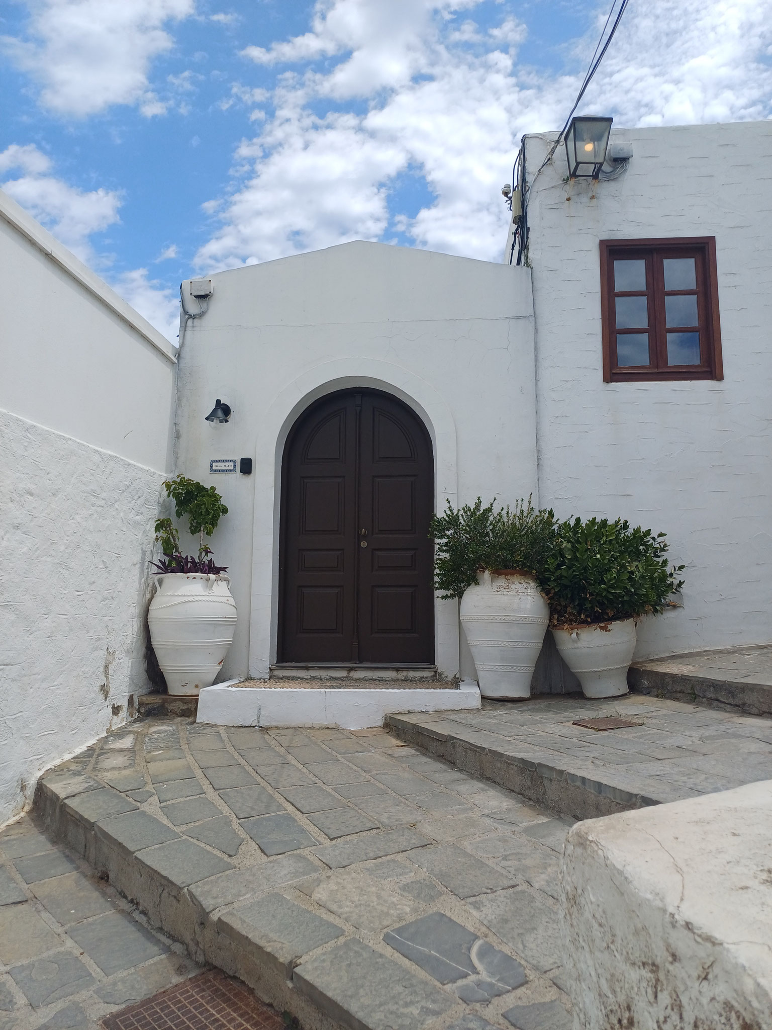 Ein weißes Haus in Lindos mit dunkler Eingangstür, daneben Blumenkübel mit Pflanzen.