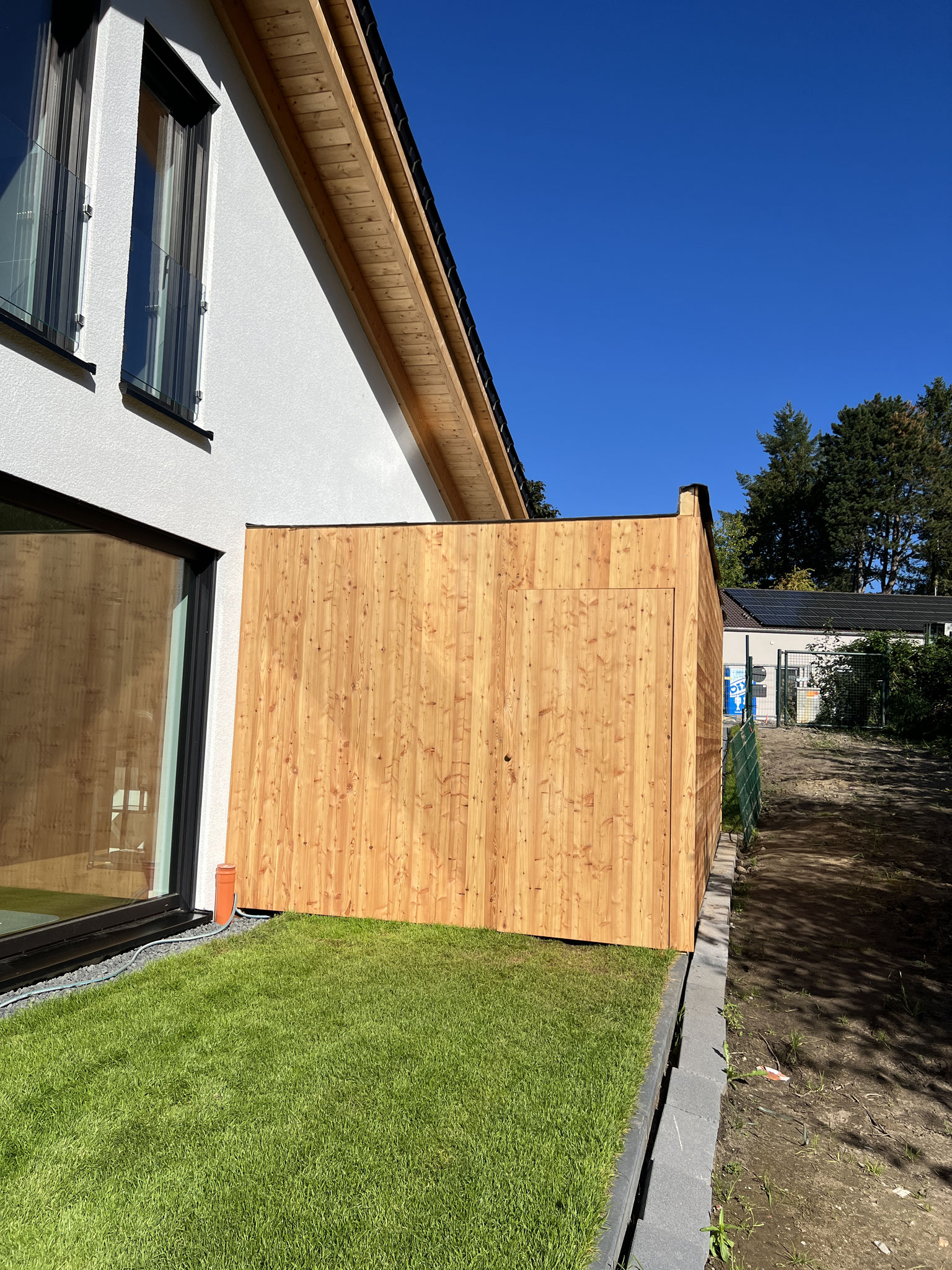 Garagenfassade aus einer Naturholzplatte Lärche mit einer integrierten Tür