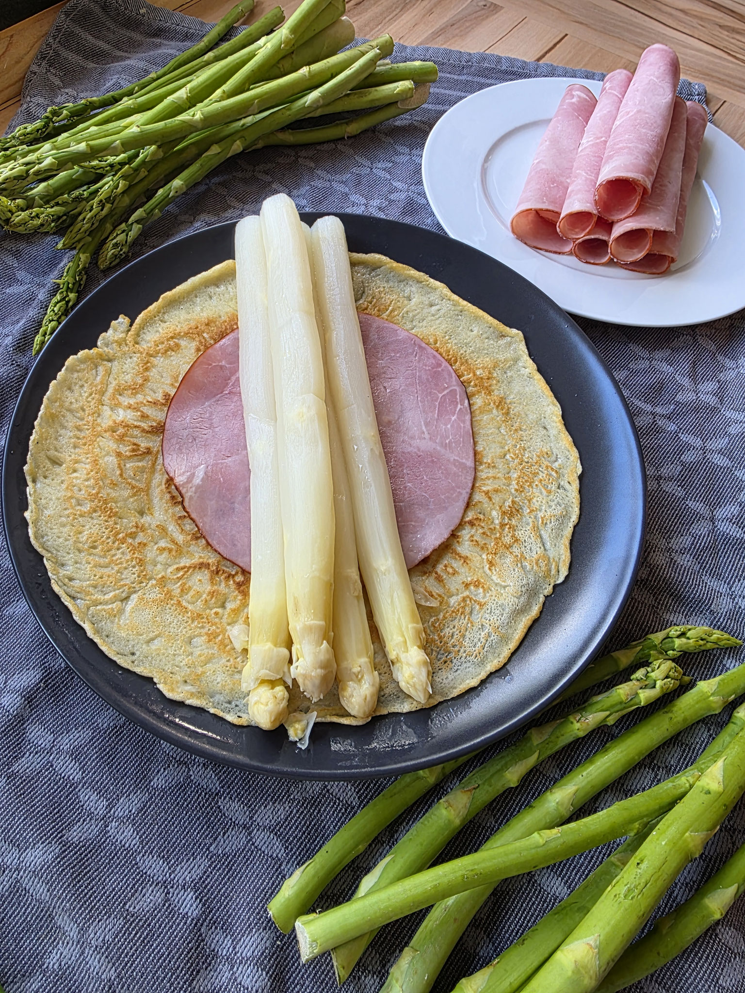 Pfannkuchen auf dem Teller belegt mit Schinken und Spargel bereit zum Rollen