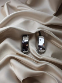 Shiny silver hoop earrings placed on softly folded champagne-colored silk. Minimalist product photo with focus on the smooth polished surface.