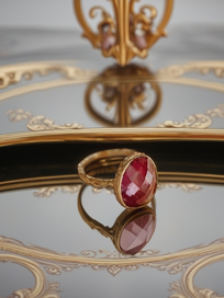 MOKOŠEV luxury jewelry, gold ring with a faceted red crystal on a decorative mirror with golden details.