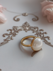 MOKOŠEV luxury jewelry, gold ring with a large shimmering pearl on a decorative light surface.
