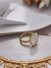 MOKOŠEV Luxusschmuck, goldener Ring mit hell schimmerndem Stein auf dekorativem Spiegeltablett.