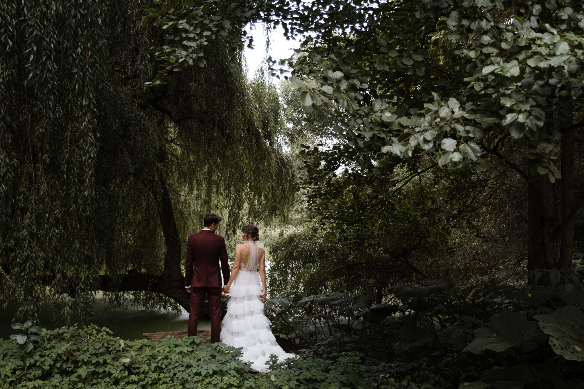 Ein Brautpaar hält sich an den Händen und schaut sich verliebt in die Augen, sie drehen der Kamera den Rücken zu – im Garten nach ihrer nachhaltigen Green Wedding mit Constanze Marienfeld in Hamburg