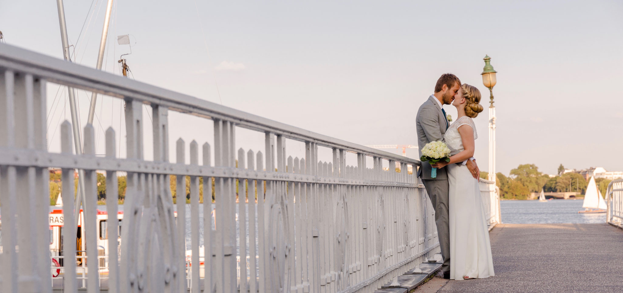 Hochzeitspaar im innigen Kuss an eine Brücke gelehnt auf der Hamburger Außenalster – Freie Trauung mit Constanze Marienfeld