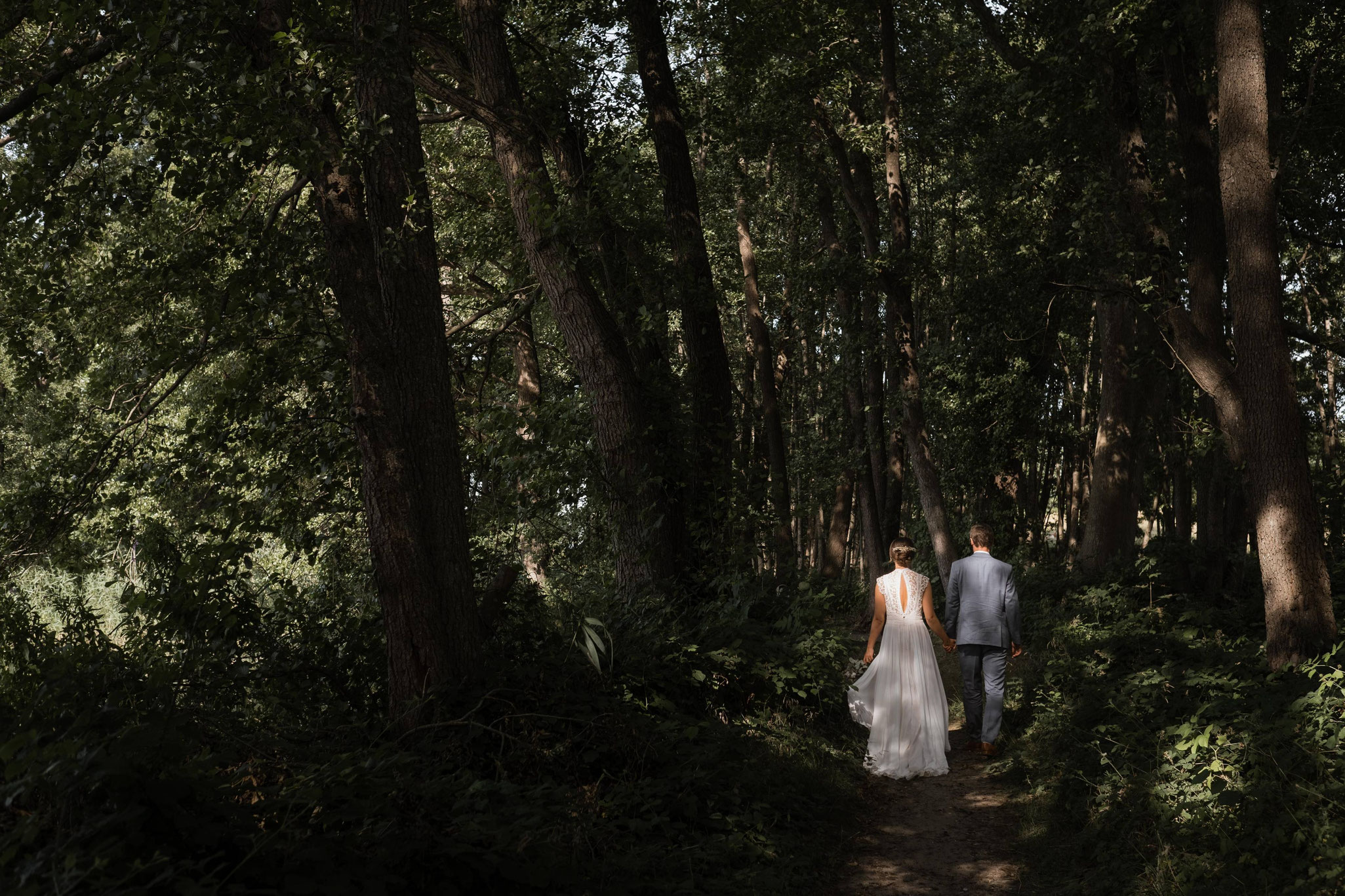 Ein Brautpaar hält sich an den Händen und geht durch den Wald.