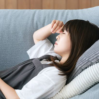 疲れて自宅ソファーで横になり目を閉じる中年主婦