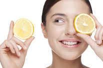 Frau hält Zitronenscheiben vor ihre Augen. Fruchtsäure als Peeling.