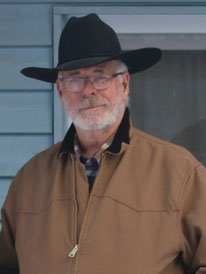 Bruce lächelt in die Kamera. Er trägt einen schwarzen Cowboyhut.