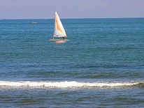 Segelboot mit weißem Segel und orangefarbenem Muster auf ruhigem Meer